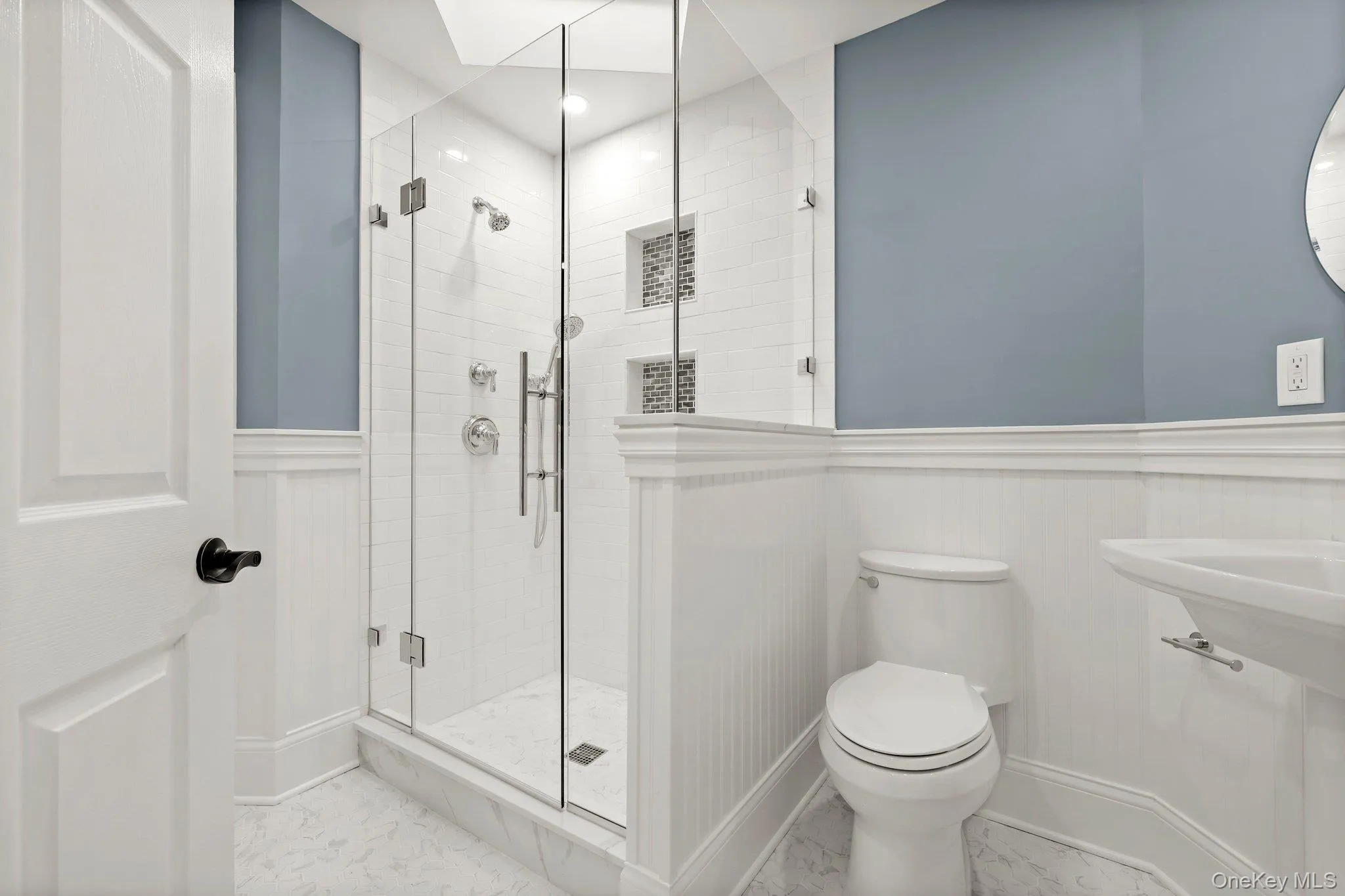 Full bath featuring marble finish flooring, wainscoting, toilet, a stall shower, and a decorative wall Full bath featuring marble finish flooring, wainscoting, toilet, a stall shower, and a decorative wall