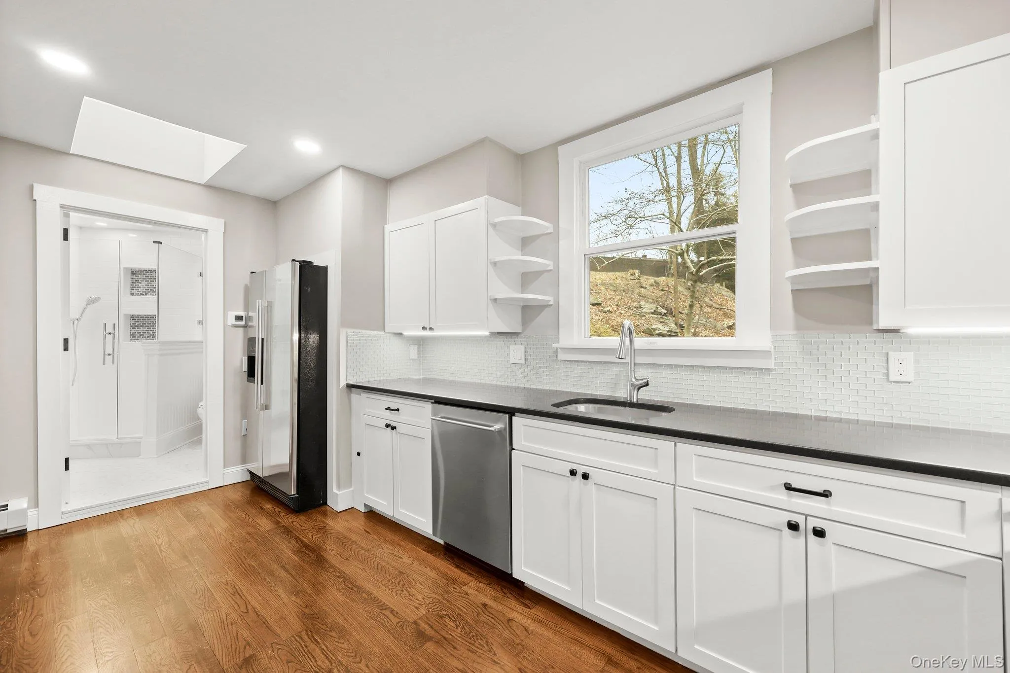 Kitchen with open shelves, stainless steel appliances, a sink, dark countertops, and a skylight Kitchen with open shelves, stainless steel appliances, a sink, dark countertops, and a skylight