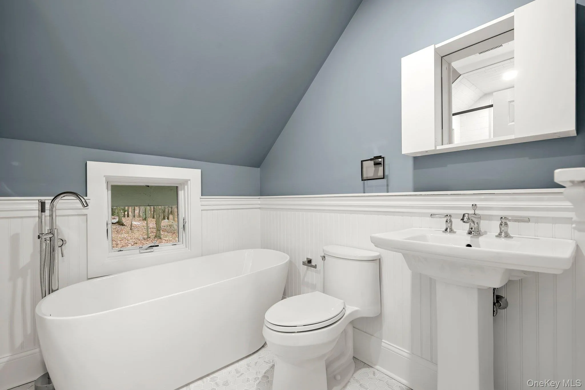 Full bathroom featuring marble finish flooring, a freestanding tub, lofted ceiling, a wainscoted wall, and toilet Full bathroom featuring marble finish flooring, a freestanding tub, lofted ceiling, a wainscoted wall, and toilet