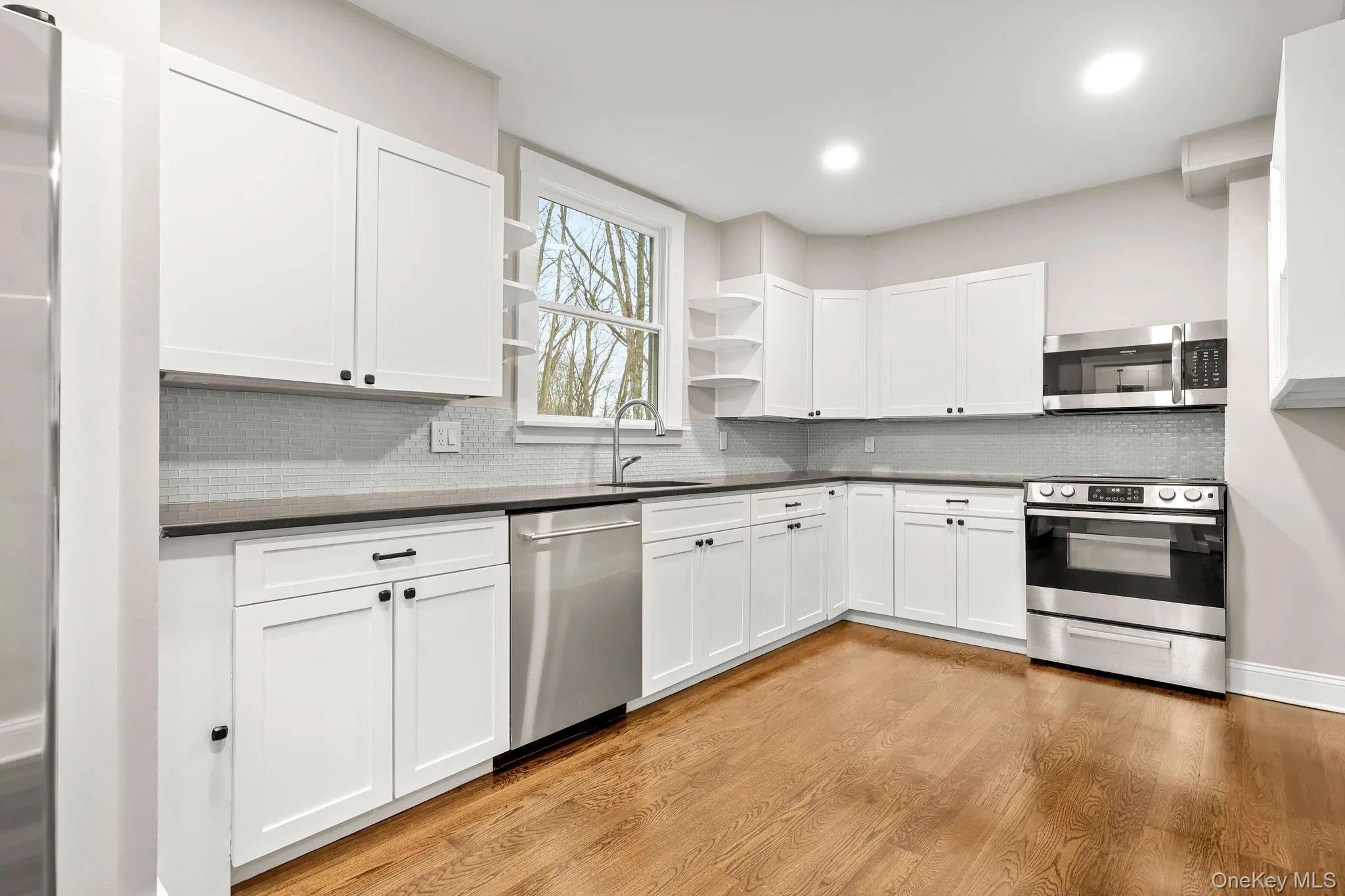 Kitchen featuring stainless steel appliances, open shelves, a sink, dark countertops, and  wood floors Kitchen featuring stainless steel appliances, open shelves, a sink, dark countertops, and  wood floors