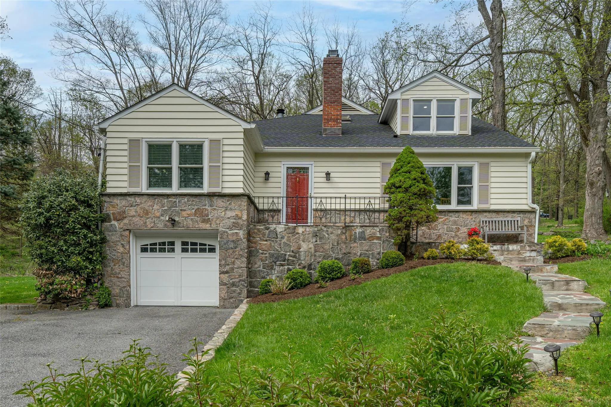 View of front of house featuring stone siding, a chimney, a garage, a front lawn, and driveway View of front of house featuring stone siding, a chimney, a garage, a front lawn, and driveway