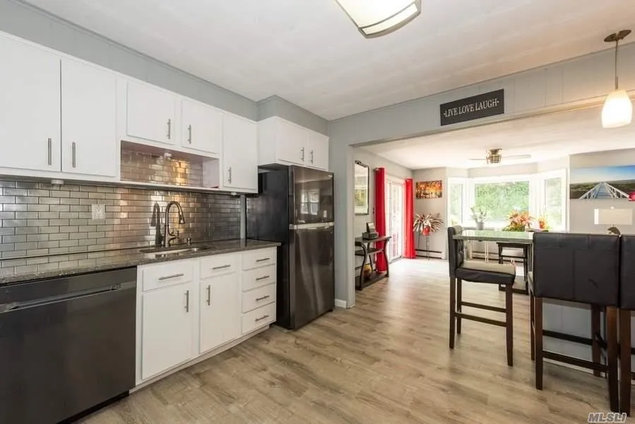 Kitchen featuring dishwasher, a sink, freestanding refrigerator, a baseboard heating unit, and backsplash Kitchen featuring dishwasher, a sink, freestanding refrigerator, a baseboard heating unit, and backsplash