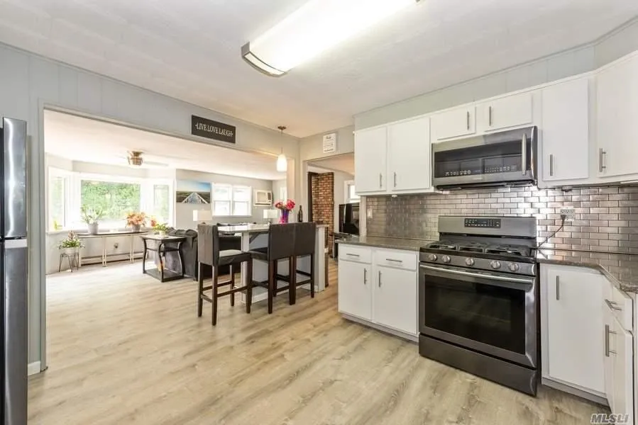 Kitchen with appliances with stainless steel finishes, light wood finished floors, white cabinets, tasteful backsplash, and dark stone counters Kitchen with appliances with stainless steel finishes, light wood finished floors, white cabinets, tasteful backsplash, and dark stone counters