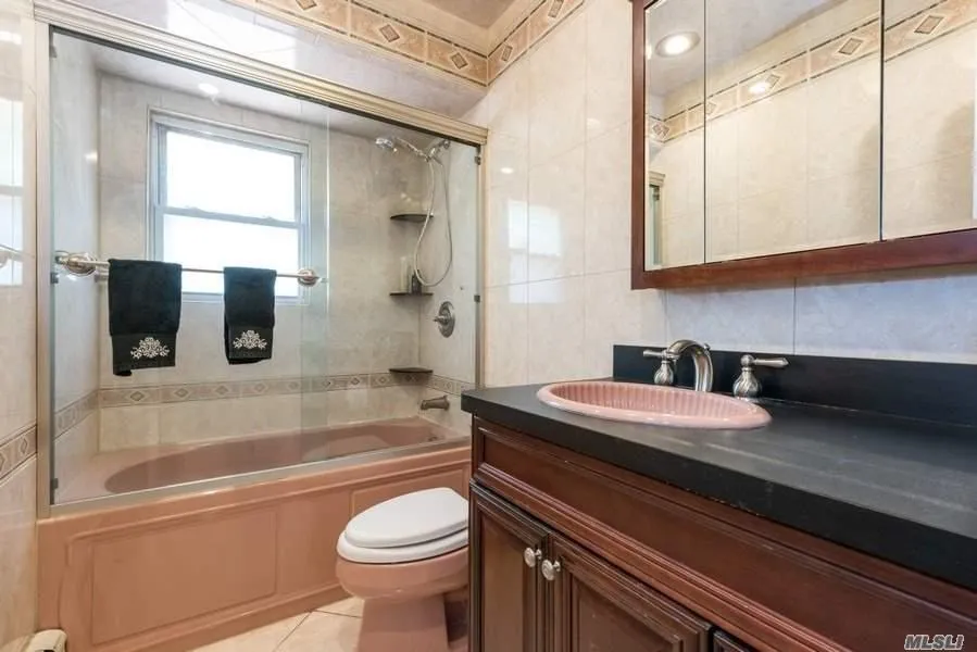 Bathroom with toilet, vanity, bathing tub / shower combination, tile patterned floors, and tile walls Bathroom with toilet, vanity, bathing tub / shower combination, tile patterned floors, and tile walls