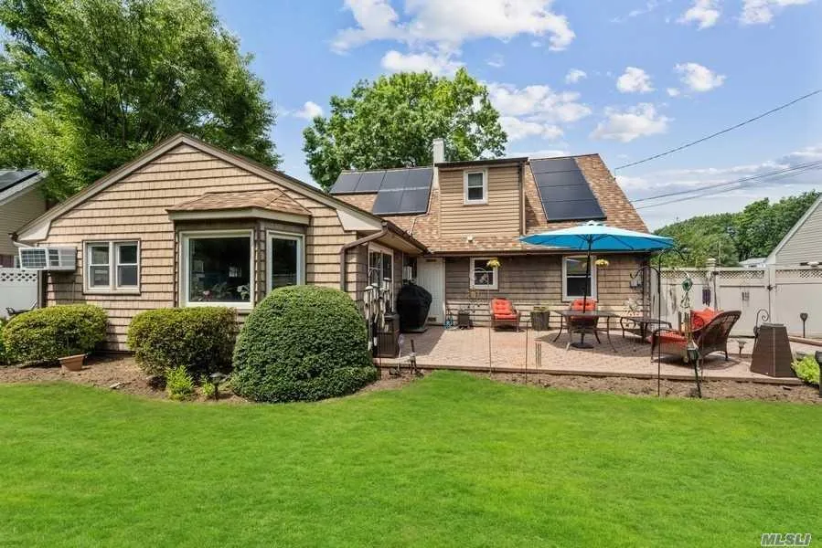 Rear view of property with roof mounted solar panels and a patio area Rear view of property with roof mounted solar panels and a patio area