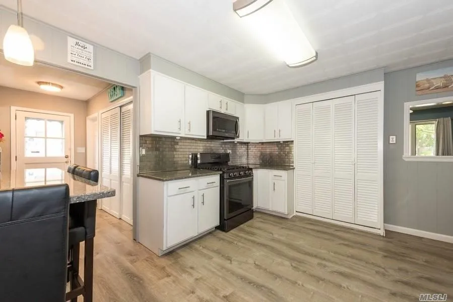 Kitchen featuring stainless steel appliances, light wood-style flooring, white cabinets, and decorative backsplash Kitchen featuring stainless steel appliances, light wood-style flooring, white cabinets, and decorative backsplash