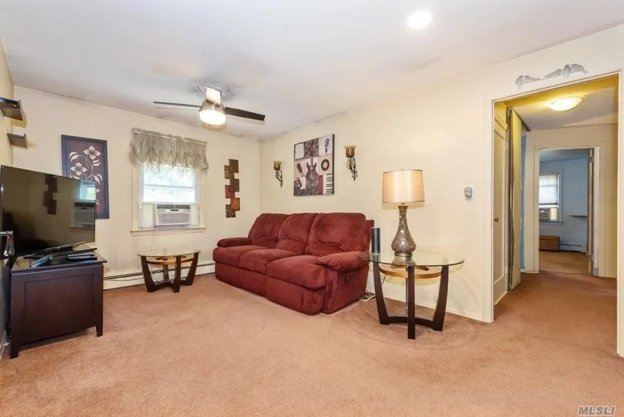 Living area featuring light colored carpet, a baseboard radiator, cooling unit, baseboards, and a ceiling fan Living area featuring light colored carpet, a baseboard radiator, cooling unit, baseboards, and a ceiling fan