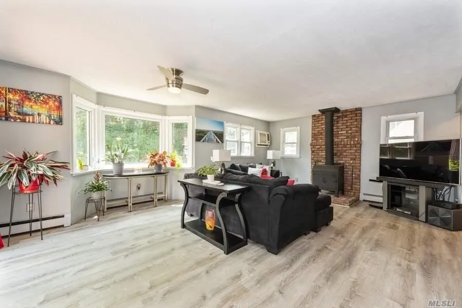 Living room featuring a wood stove, a ceiling fan, a baseboard heating unit, and wood finished floors Living room featuring a wood stove, a ceiling fan, a baseboard heating unit, and wood finished floors