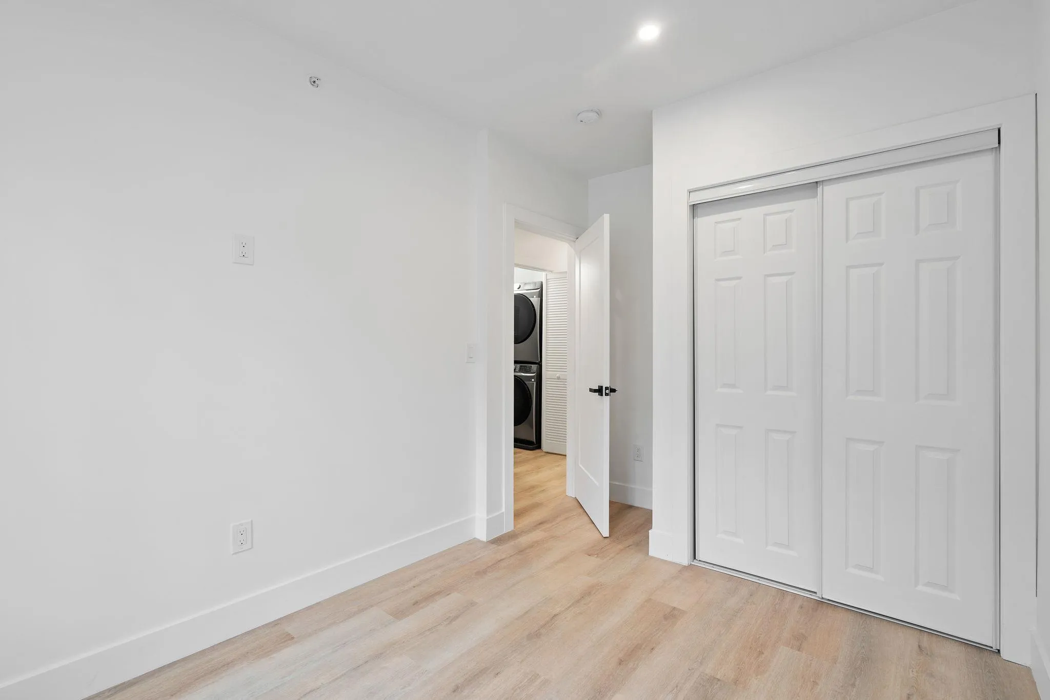 Unfurnished bedroom with stacked washer and dryer, a closet, and light hardwood / wood-style floors Unfurnished bedroom with stacked washer and dryer, a closet, and light hardwood / wood-style floors