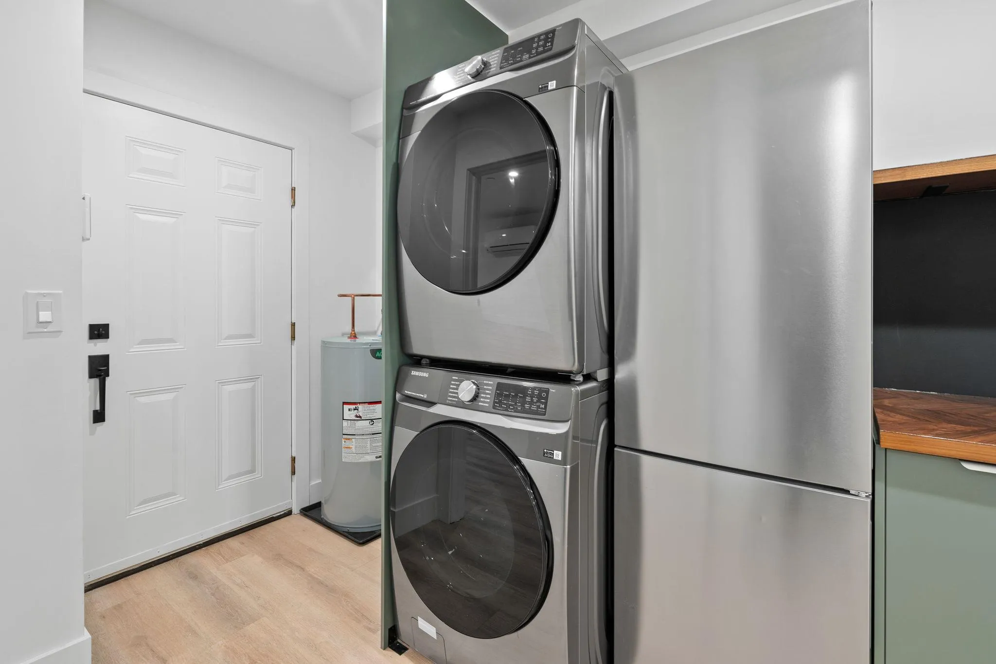 Washroom featuring stacked washer / dryer, electric water heater, and light hardwood / wood-style floors Washroom featuring stacked washer / dryer, electric water heater, and light hardwood / wood-style floors