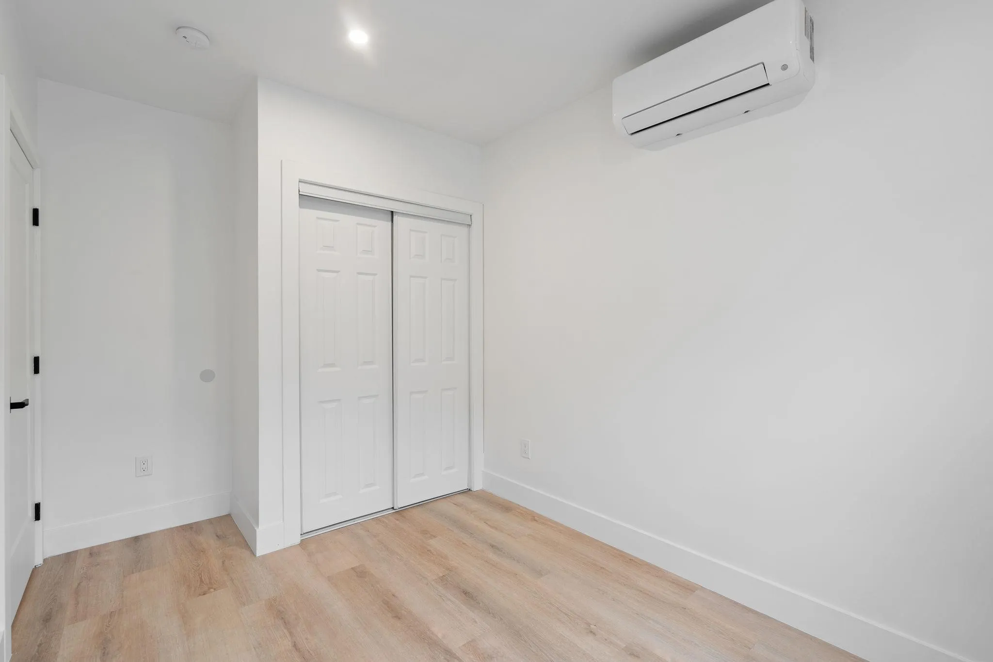 Unfurnished bedroom with a wall unit AC, a closet, and light hardwood / wood-style floors Unfurnished bedroom with a wall unit AC, a closet, and light hardwood / wood-style floors