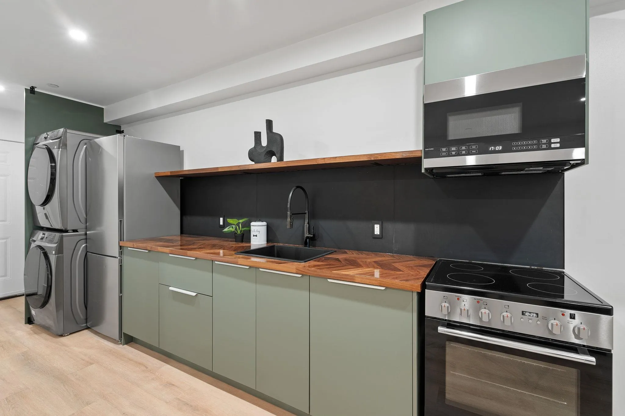 Kitchen with butcher block counters, sink, stacked washing maching and dryer, appliances with stainless steel finishes, and light wood-type flooring Kitchen with butcher block counters, sink, stacked washing maching and dryer, appliances with stainless steel finishes, and light wood-type flooring