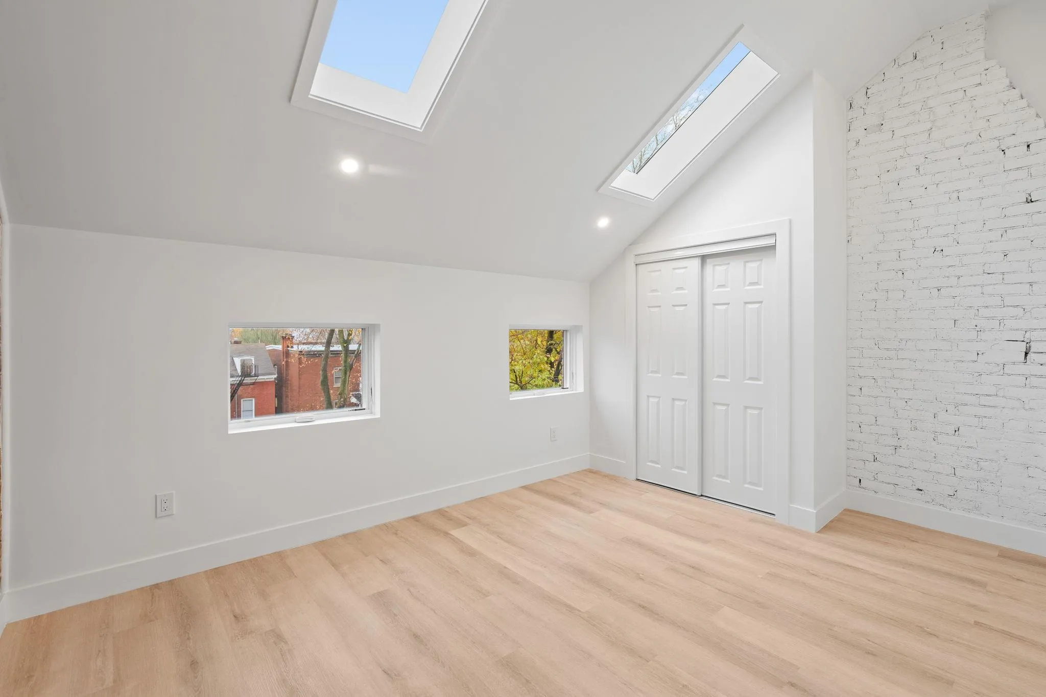 Unfurnished bedroom with light hardwood / wood-style floors, lofted ceiling with skylight, brick wall, and a closet Unfurnished bedroom with light hardwood / wood-style floors, lofted ceiling with skylight, brick wall, and a closet