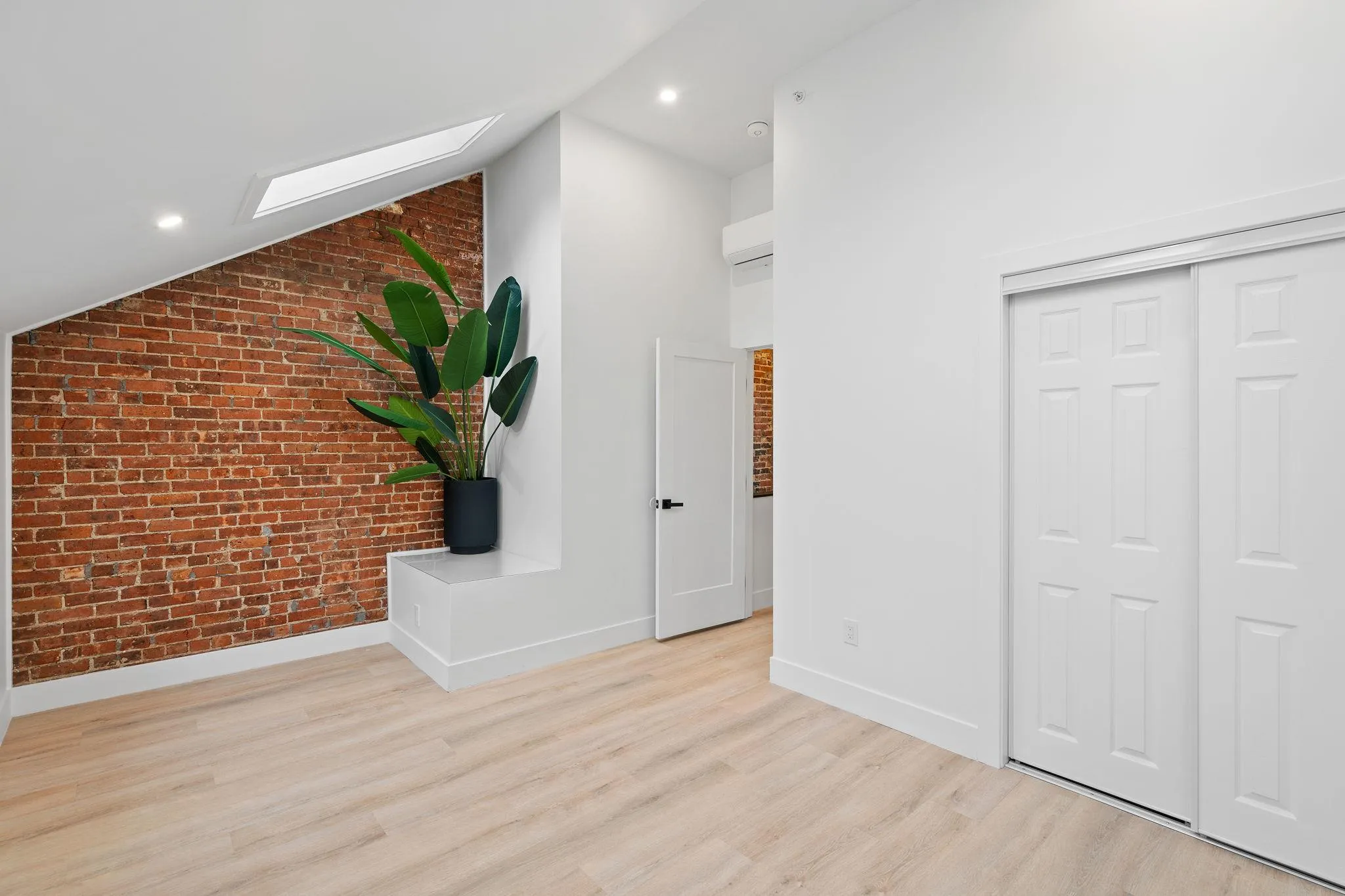 Corridor featuring light wood-type flooring, vaulted ceiling with skylight, and brick wall Corridor featuring light wood-type flooring, vaulted ceiling with skylight, and brick wall
