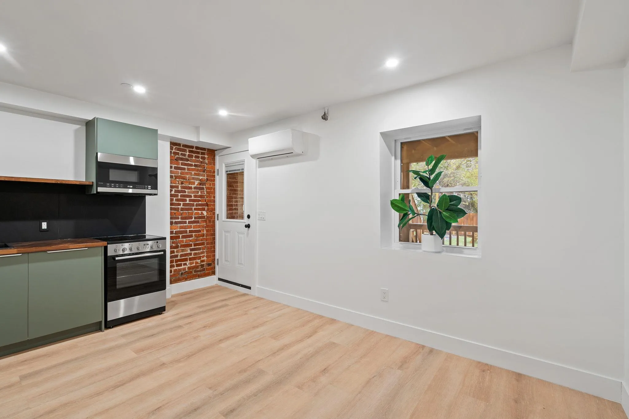Kitchen featuring a wall mounted air conditioner, appliances with stainless steel finishes, light wood-type flooring, and green cabinets Kitchen featuring a wall mounted air conditioner, appliances with stainless steel finishes, light wood-type flooring, and green cabinets