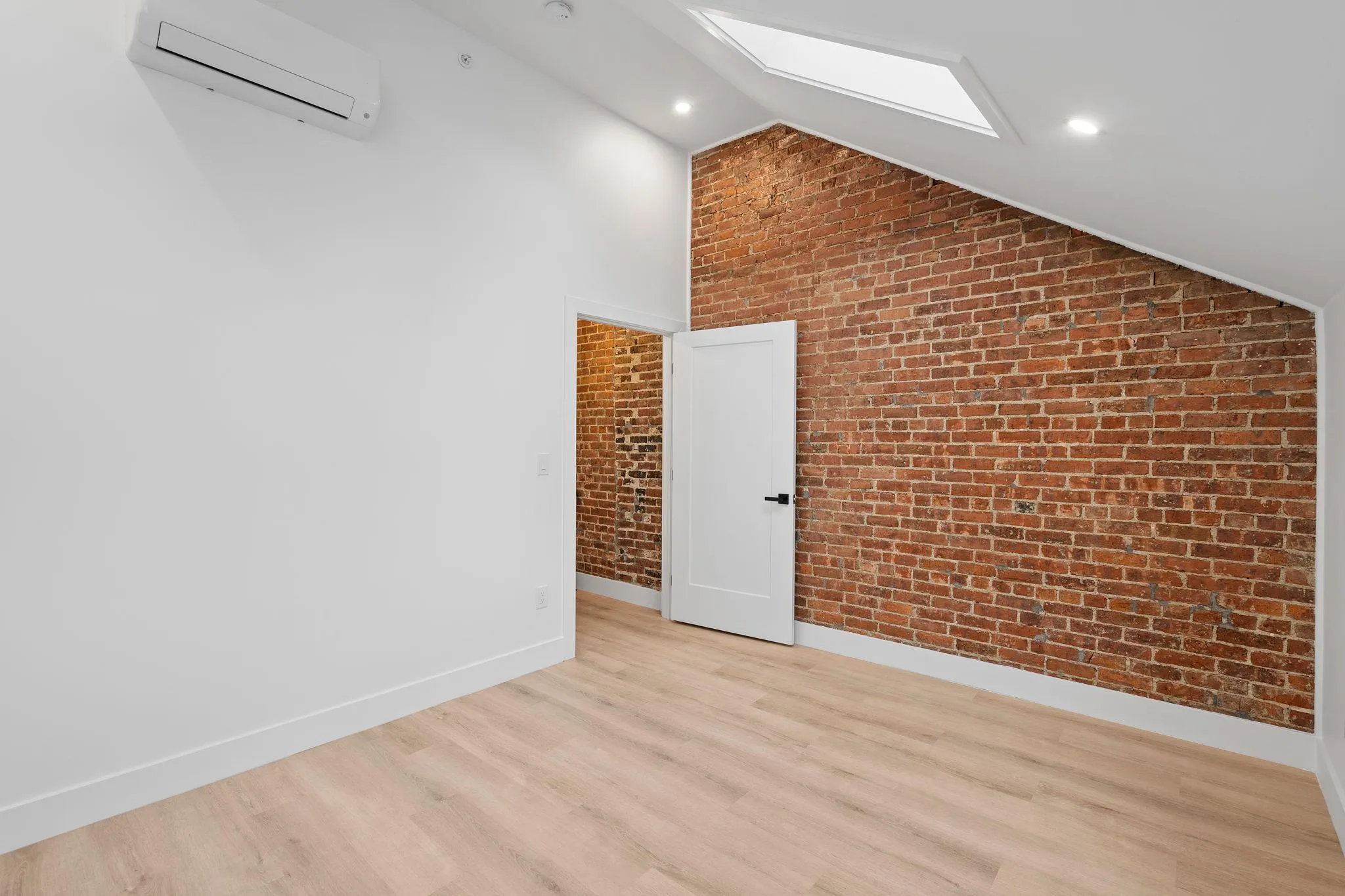 Bonus room with vaulted ceiling with skylight, light hardwood / wood-style floors, an AC wall unit, and brick wall Bonus room with vaulted ceiling with skylight, light hardwood / wood-style floors, an AC wall unit, and brick wall