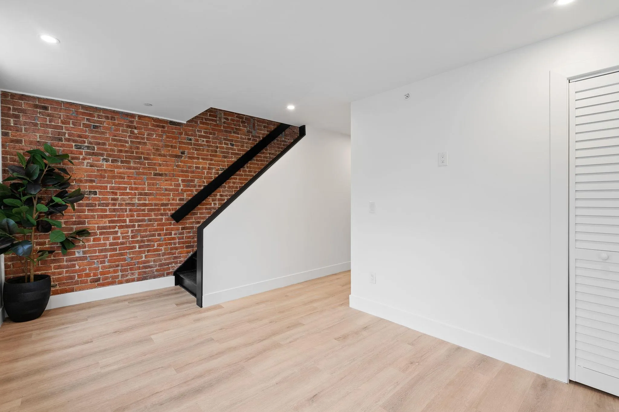 Unfurnished living room featuring brick wall and light hardwood / wood-style flooring Unfurnished living room featuring brick wall and light hardwood / wood-style flooring