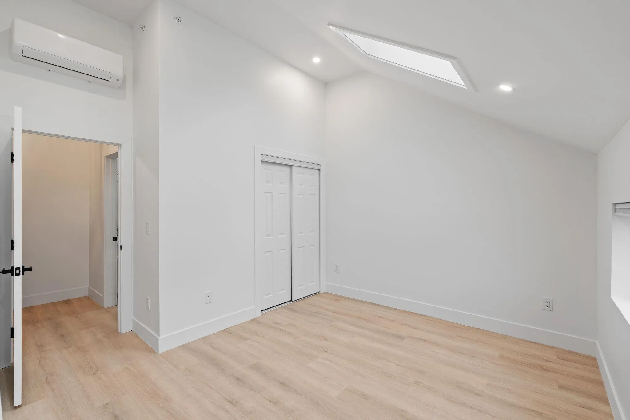 Unfurnished bedroom with high vaulted ceiling, light hardwood / wood-style floors, a wall unit AC, and a closet Unfurnished bedroom with high vaulted ceiling, light hardwood / wood-style floors, a wall unit AC, and a closet
