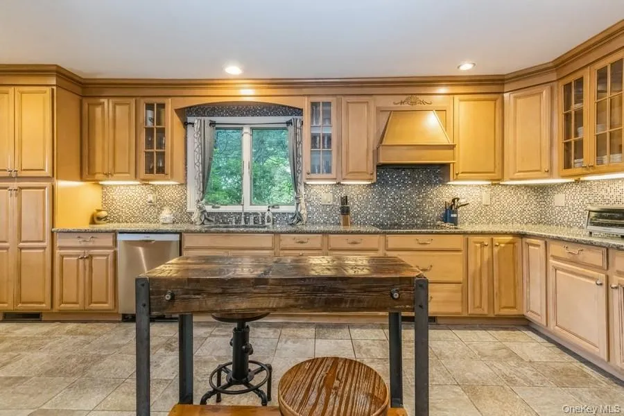 Kitchen featuring dishwasher, premium range hood, stone countertops, glass insert cabinets, and decorative backsplash Kitchen featuring dishwasher, premium range hood, stone countertops, glass insert cabinets, and decorative backsplash