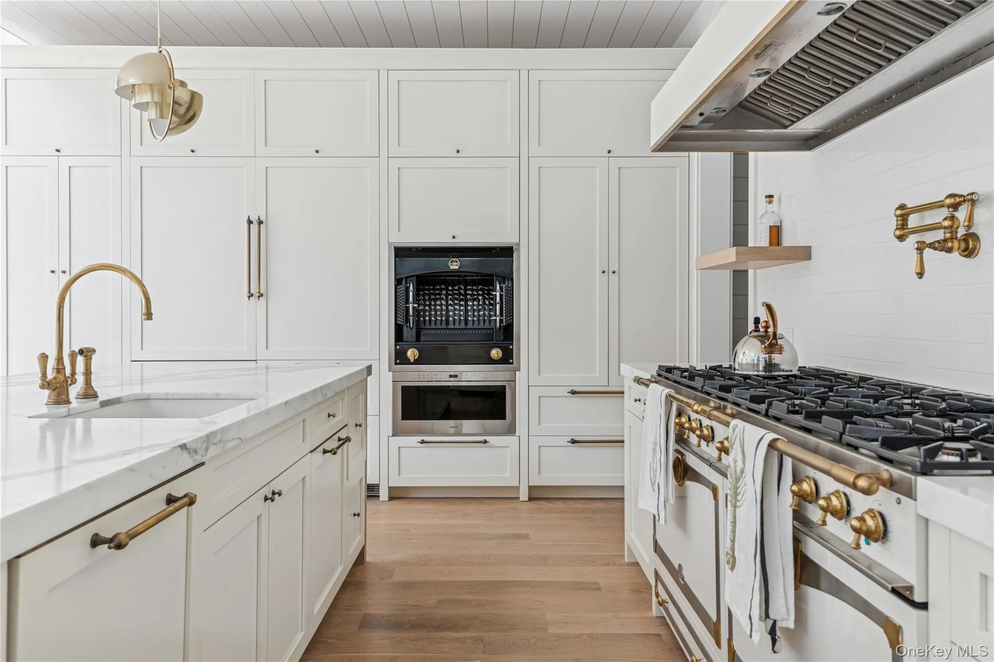 Kitchen featuring light stone counters, ventilation hood, high end stove, and white cabinetry Kitchen featuring light stone counters, ventilation hood, high end stove, and white cabinetry
