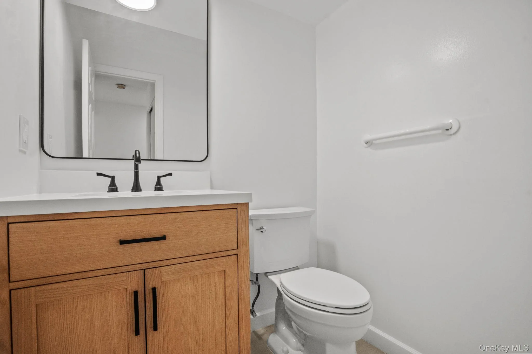 The renovated half bath features a sleek wood vanity with matte black fixtures and a contemporary framed mirror. The renovated half bath features a sleek wood vanity with matte black fixtures and a contemporary framed mirror.