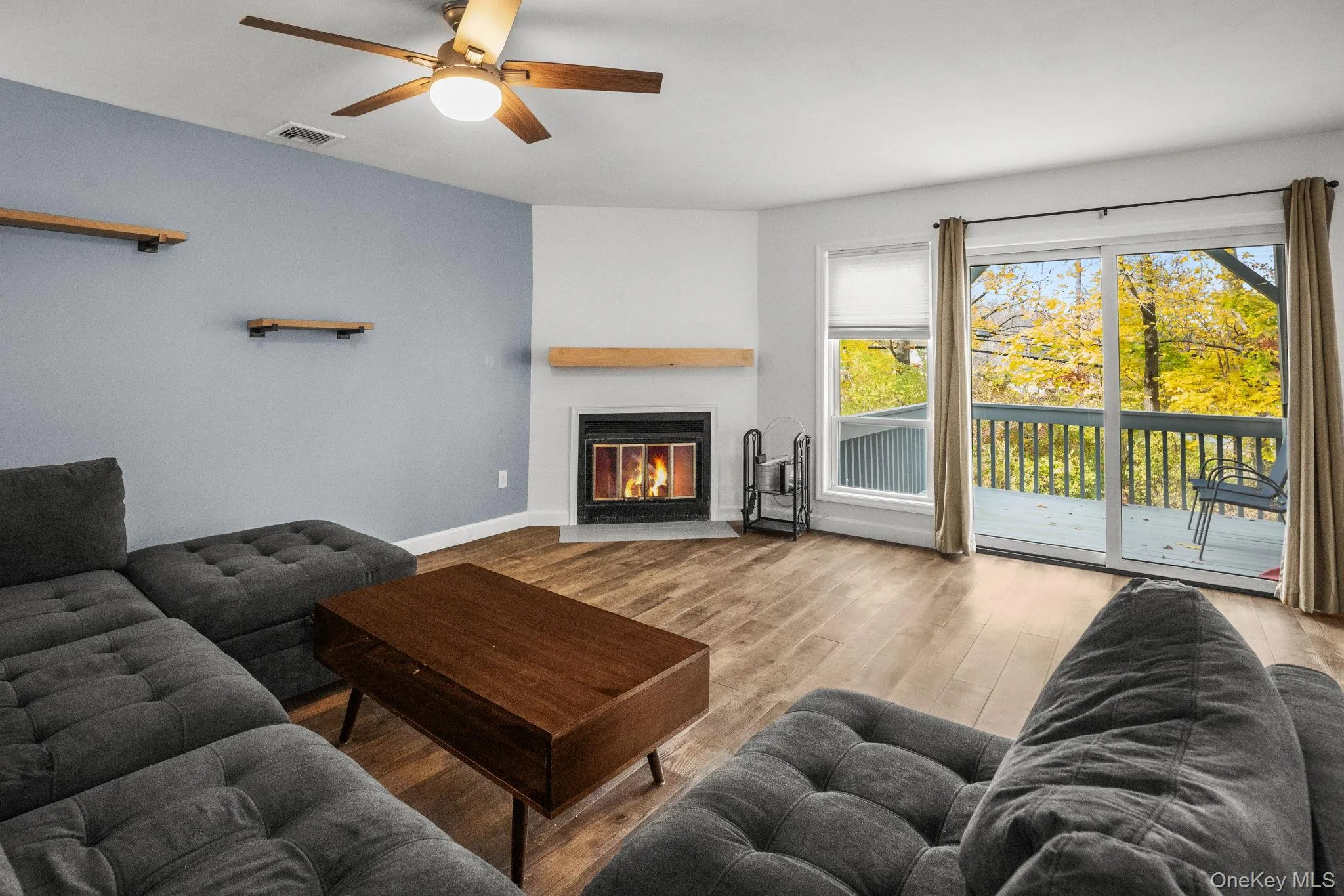 The sun-filled living room showcases a cozy wood-burning fireplace, new flooring, and sliding doors to the private deck with wooded views. The sun-filled living room showcases a cozy wood-burning fireplace, new flooring, and sliding doors to the private deck with wooded views.