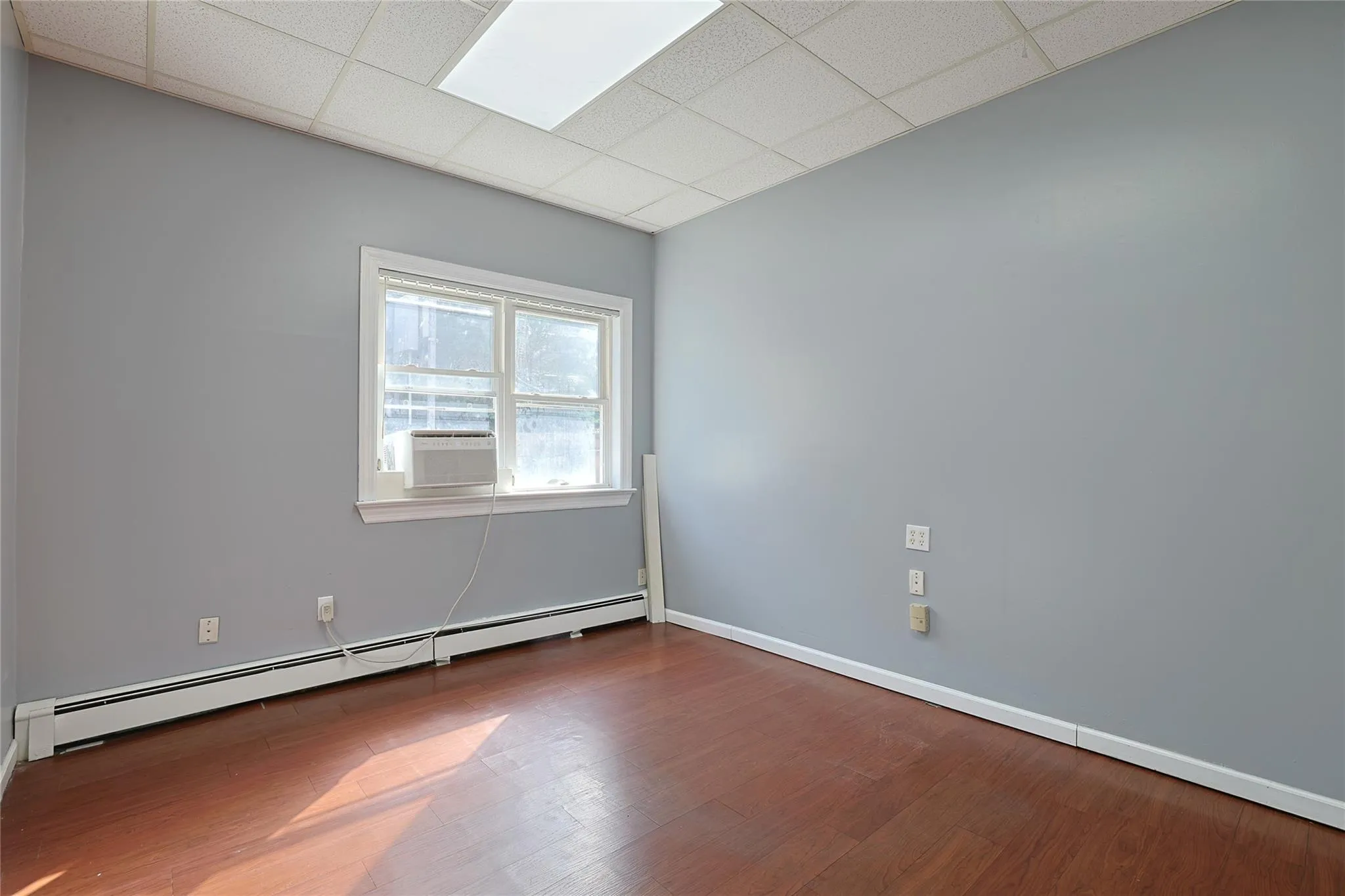 Spare room with a baseboard radiator, cooling unit, a drop ceiling, and wood finished floors Spare room with a baseboard radiator, cooling unit, a drop ceiling, and wood finished floors