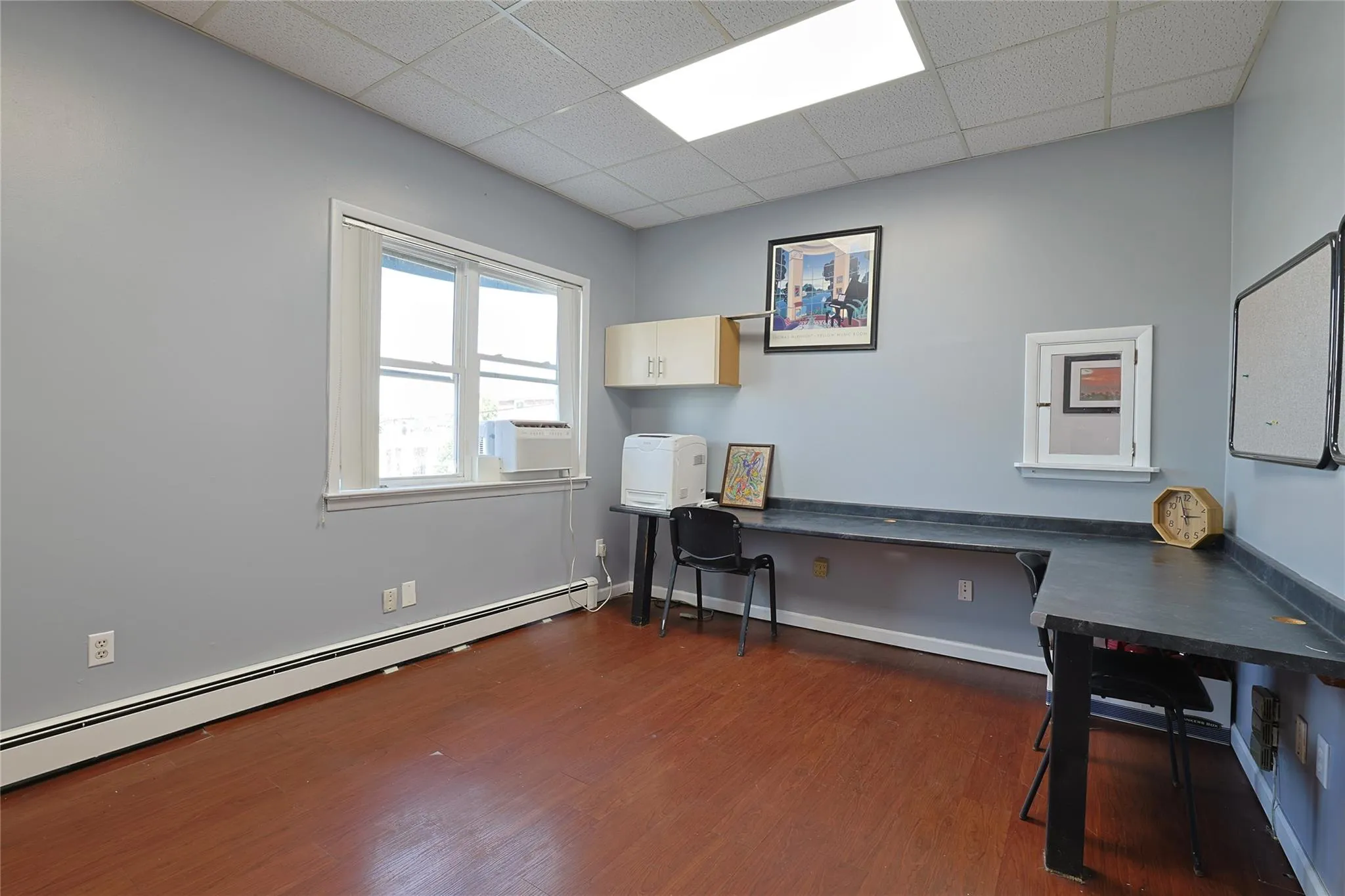 Office area featuring a baseboard radiator, a paneled ceiling, wood finished floors, built in desk, and cooling unit Office area featuring a baseboard radiator, a paneled ceiling, wood finished floors, built in desk, and cooling unit