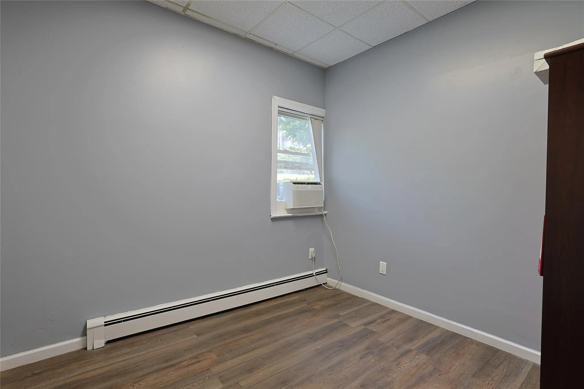 Spare room featuring baseboard heating, a drop ceiling, dark wood-style floors, and cooling unit Spare room featuring baseboard heating, a drop ceiling, dark wood-style floors, and cooling unit