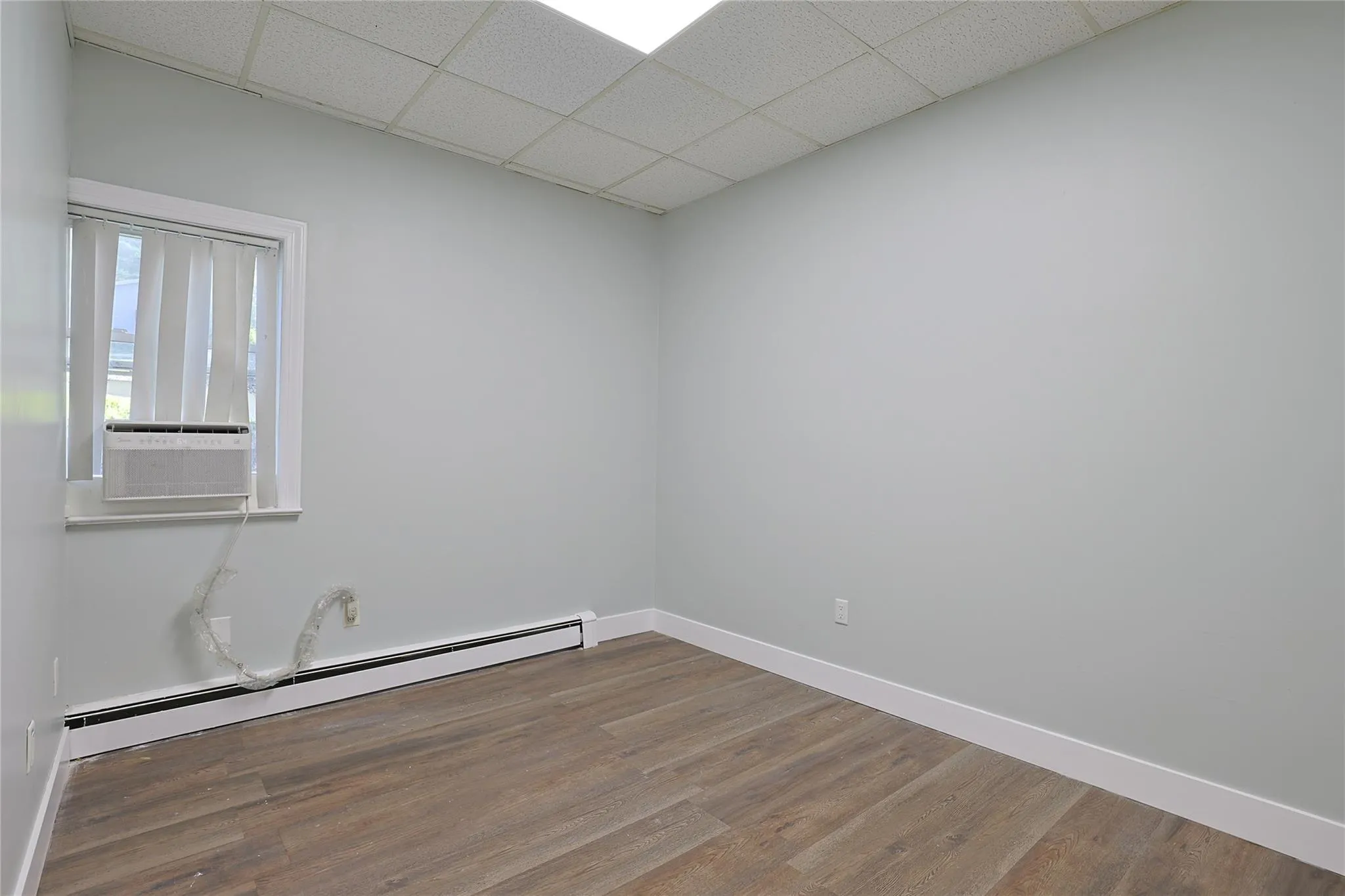 Unfurnished room with a baseboard heating unit, a paneled ceiling, wood finished floors, and cooling unit Unfurnished room with a baseboard heating unit, a paneled ceiling, wood finished floors, and cooling unit