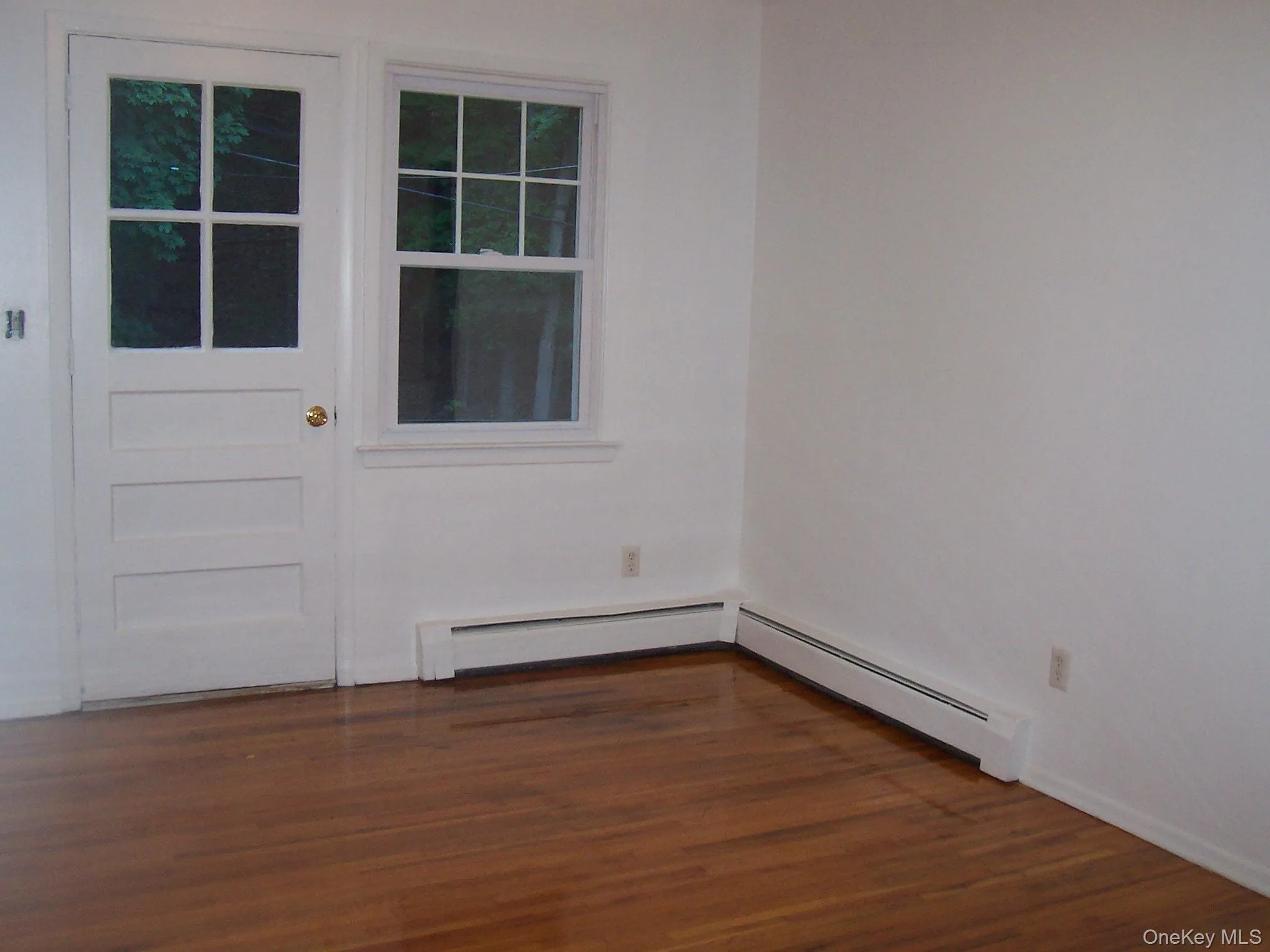 Unfurnished room with a baseboard heating unit, wood finished floors, and baseboard heating Unfurnished room with a baseboard heating unit, wood finished floors, and baseboard heating