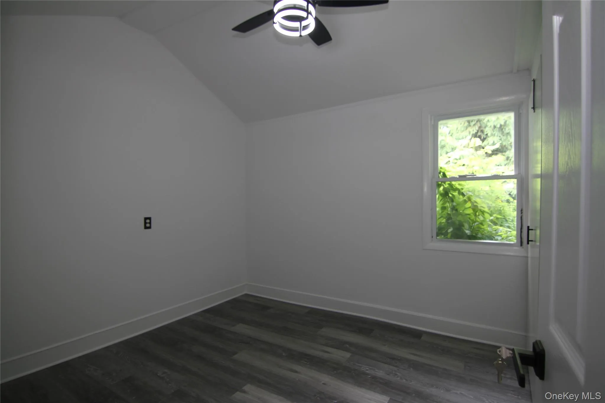 Empty room with ceiling fan, vaulted ceiling, and dark wood-type flooring Empty room with ceiling fan, vaulted ceiling, and dark wood-type flooring