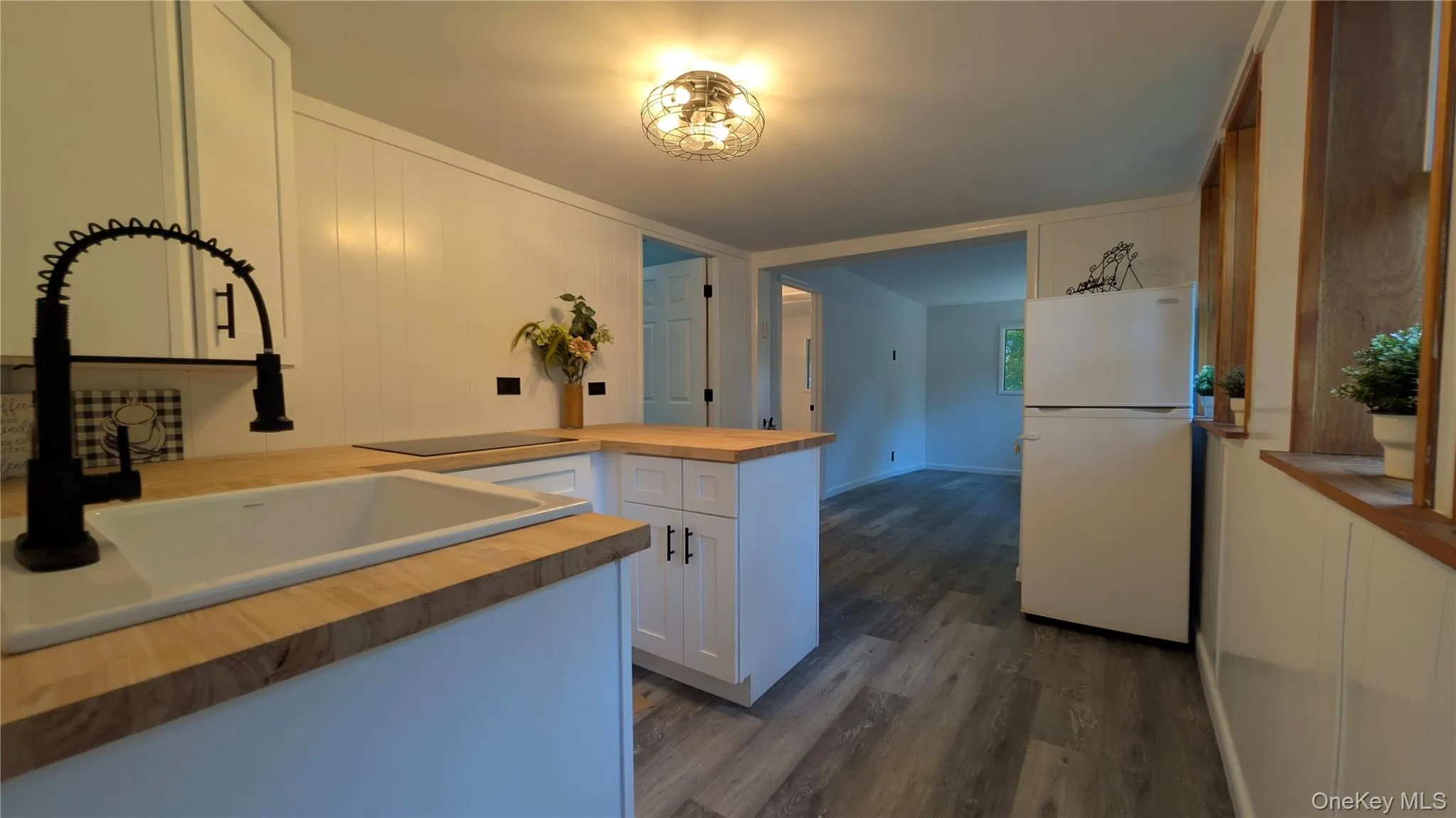 Kitchen featuring wood counters, freestanding refrigerator, a peninsula, white cabinets, and dark wood-style floors Kitchen featuring wood counters, freestanding refrigerator, a peninsula, white cabinets, and dark wood-style floors