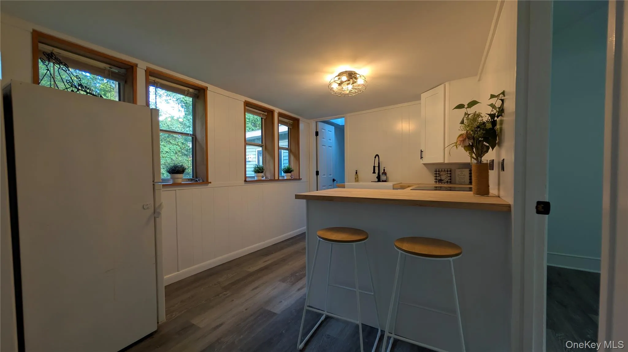 Bar area with freestanding refrigerator, white cabinets, dark wood-style floors, and light countertops Bar area with freestanding refrigerator, white cabinets, dark wood-style floors, and light countertops
