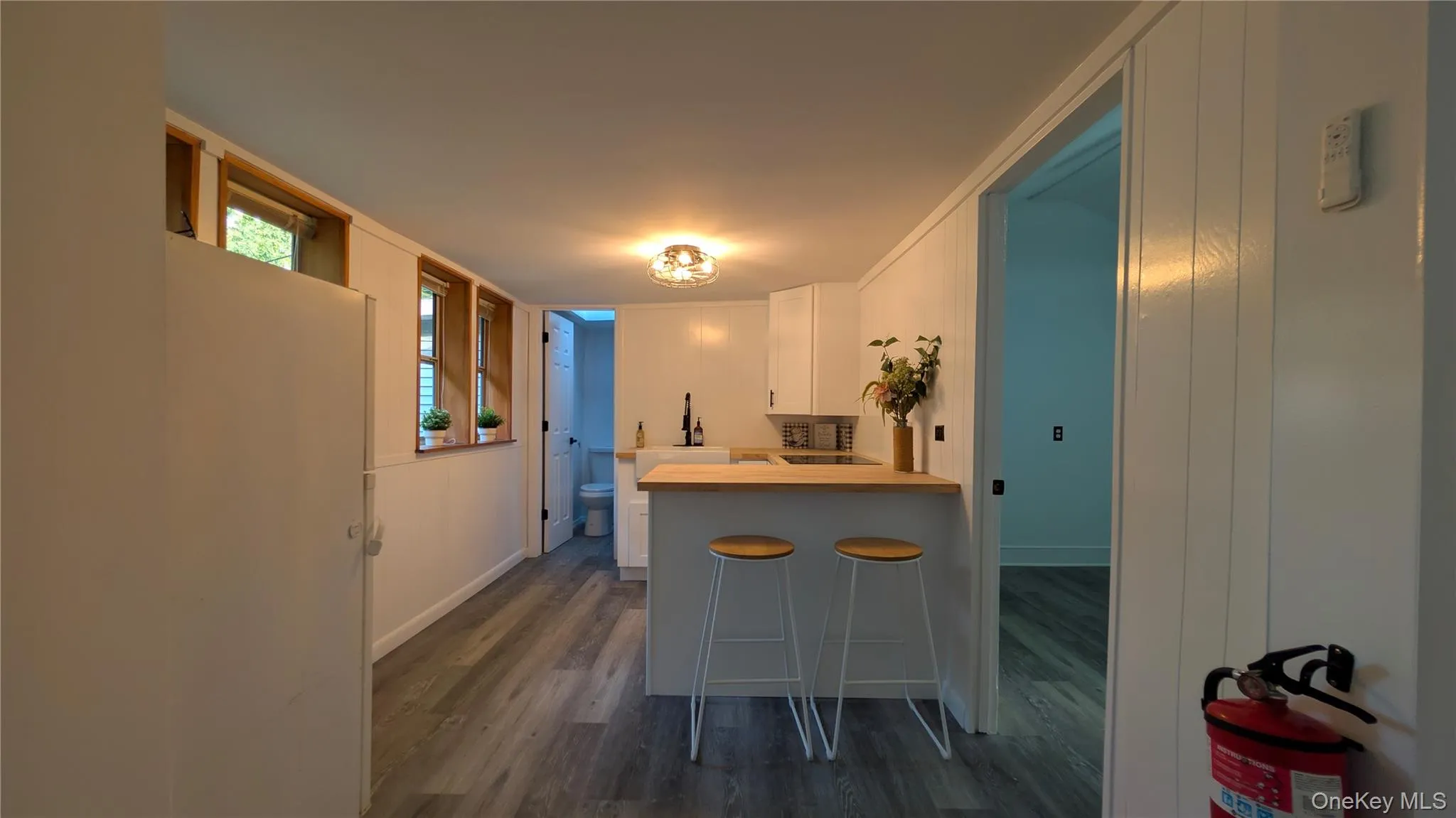 Kitchen with white cabinets, a breakfast bar, a peninsula, dark wood-style floors, and light countertops Kitchen with white cabinets, a breakfast bar, a peninsula, dark wood-style floors, and light countertops