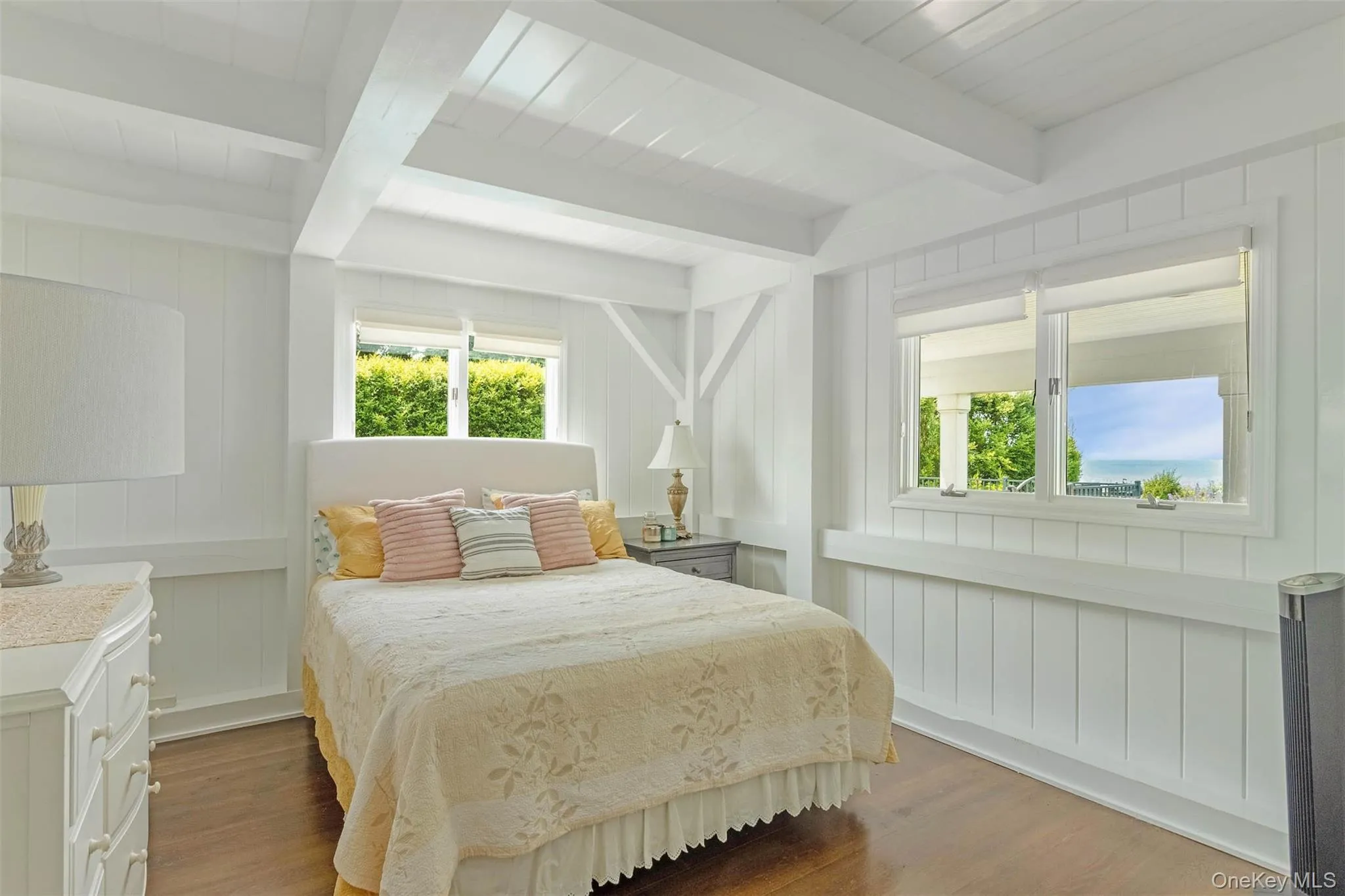 Bedroom with wood finished floors, multiple windows, beam ceiling, and a decorative wall Bedroom with wood finished floors, multiple windows, beam ceiling, and a decorative wall