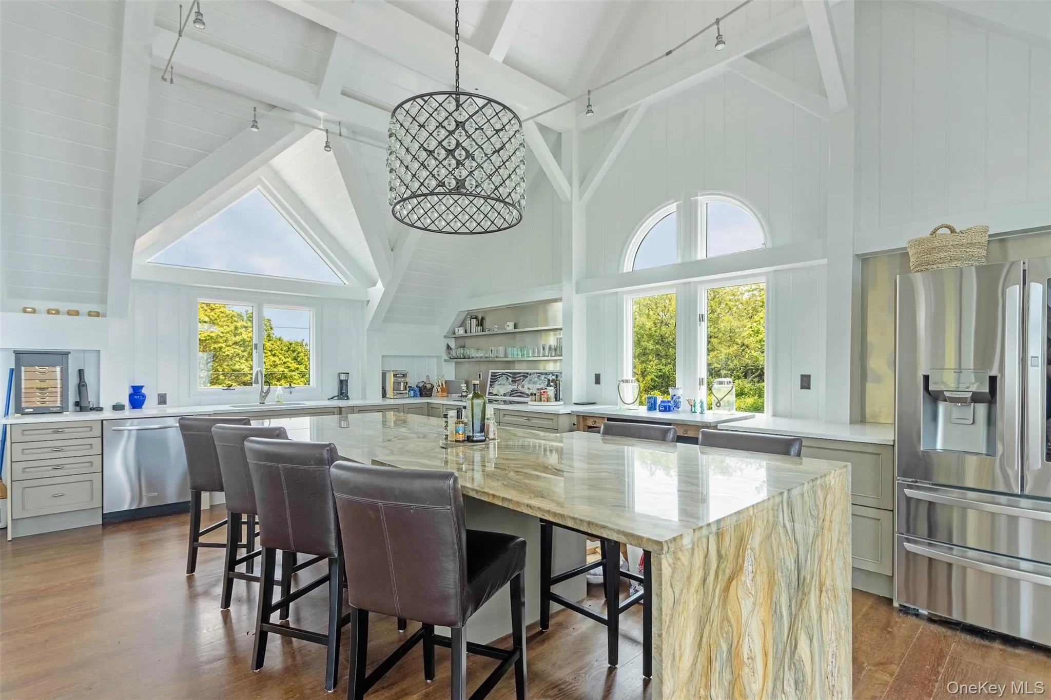 Kitchen with stainless steel appliances, high vaulted ceiling, dark wood finished floors, beam ceiling, and light stone counters Kitchen with stainless steel appliances, high vaulted ceiling, dark wood finished floors, beam ceiling, and light stone counters