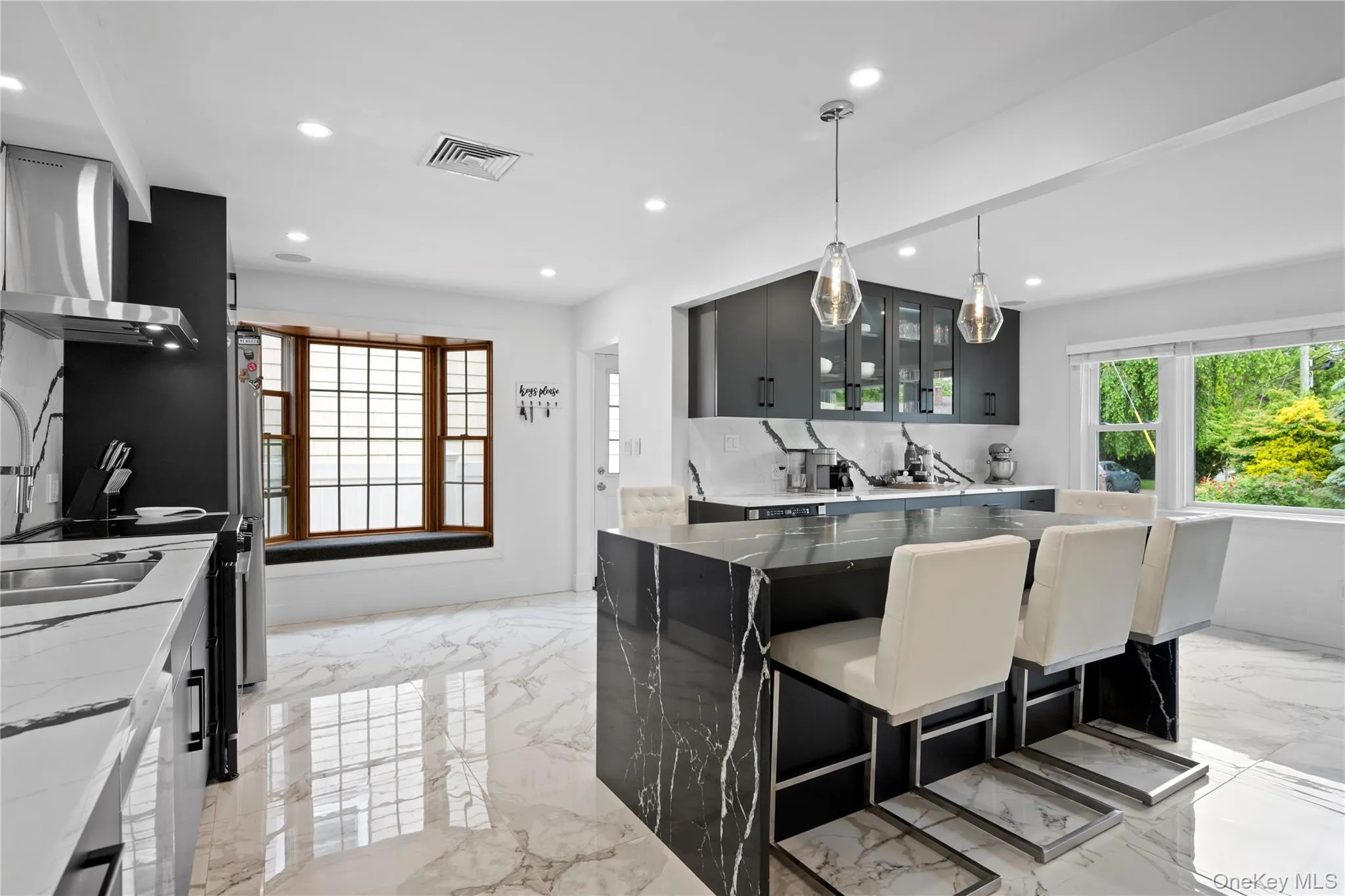 Kitchen with light marble finish flooring, recessed lighting, glass insert cabinets, pendant lighting, and wall chimney exhaust hood Kitchen with light marble finish flooring, recessed lighting, glass insert cabinets, pendant lighting, and wall chimney exhaust hood