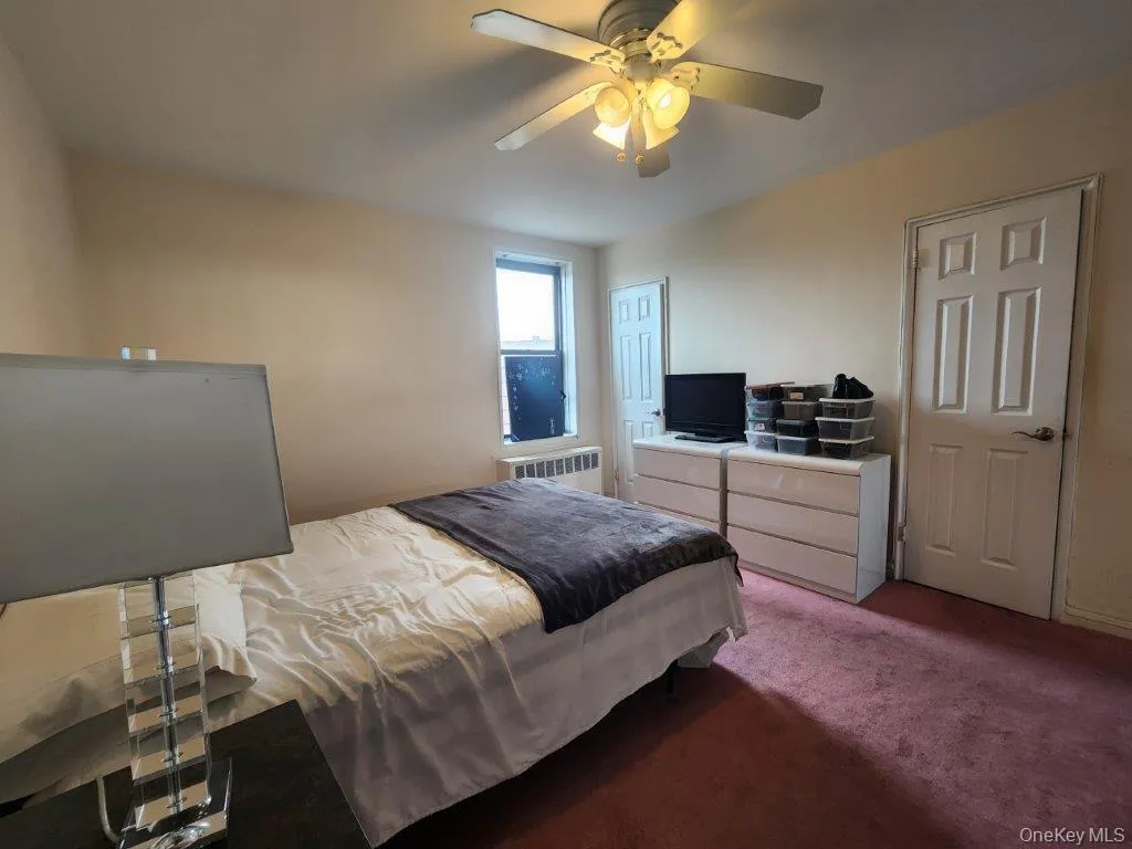 Carpeted bedroom with radiator heating unit and a ceiling fan Carpeted bedroom with radiator heating unit and a ceiling fan