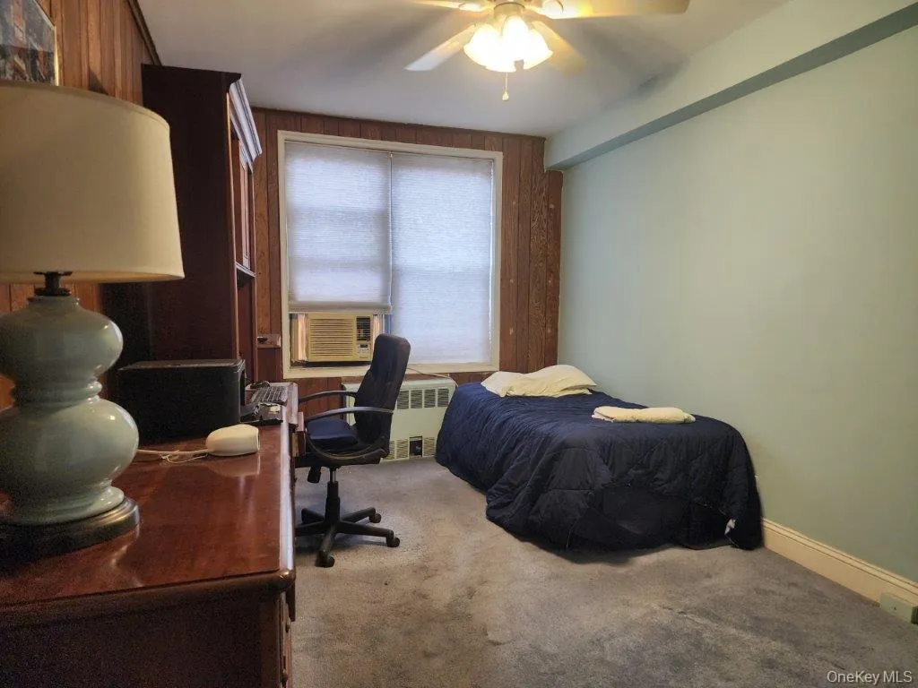 Carpeted bedroom with an office area, radiator, and a ceiling fan Carpeted bedroom with an office area, radiator, and a ceiling fan
