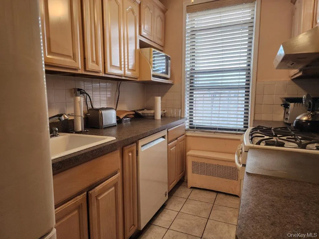 Kitchen featuring dishwasher, wall chimney exhaust hood, decorative backsplash, dark countertops, and freestanding refrigerator Kitchen featuring dishwasher, wall chimney exhaust hood, decorative backsplash, dark countertops, and freestanding refrigerator