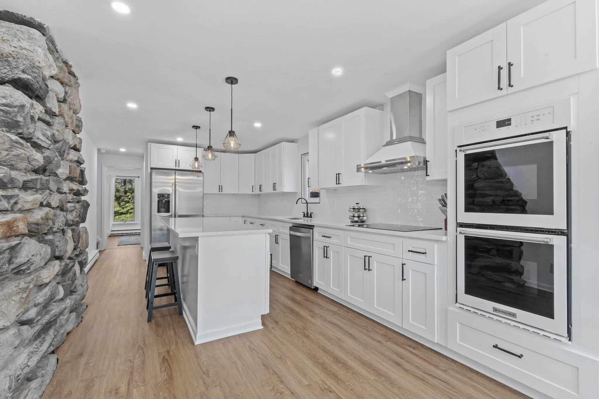 Kitchen with stainless steel appliances, wall chimney range hood, light wood-style flooring, light countertops, and a kitchen bar Kitchen with stainless steel appliances, wall chimney range hood, light wood-style flooring, light countertops, and a kitchen bar
