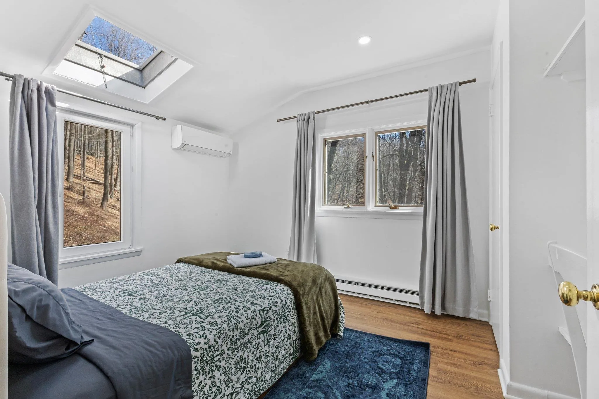 Bedroom featuring a wall mounted AC, a baseboard radiator, a skylight, vaulted ceiling, and wood finished floors Bedroom featuring a wall mounted AC, a baseboard radiator, a skylight, vaulted ceiling, and wood finished floors