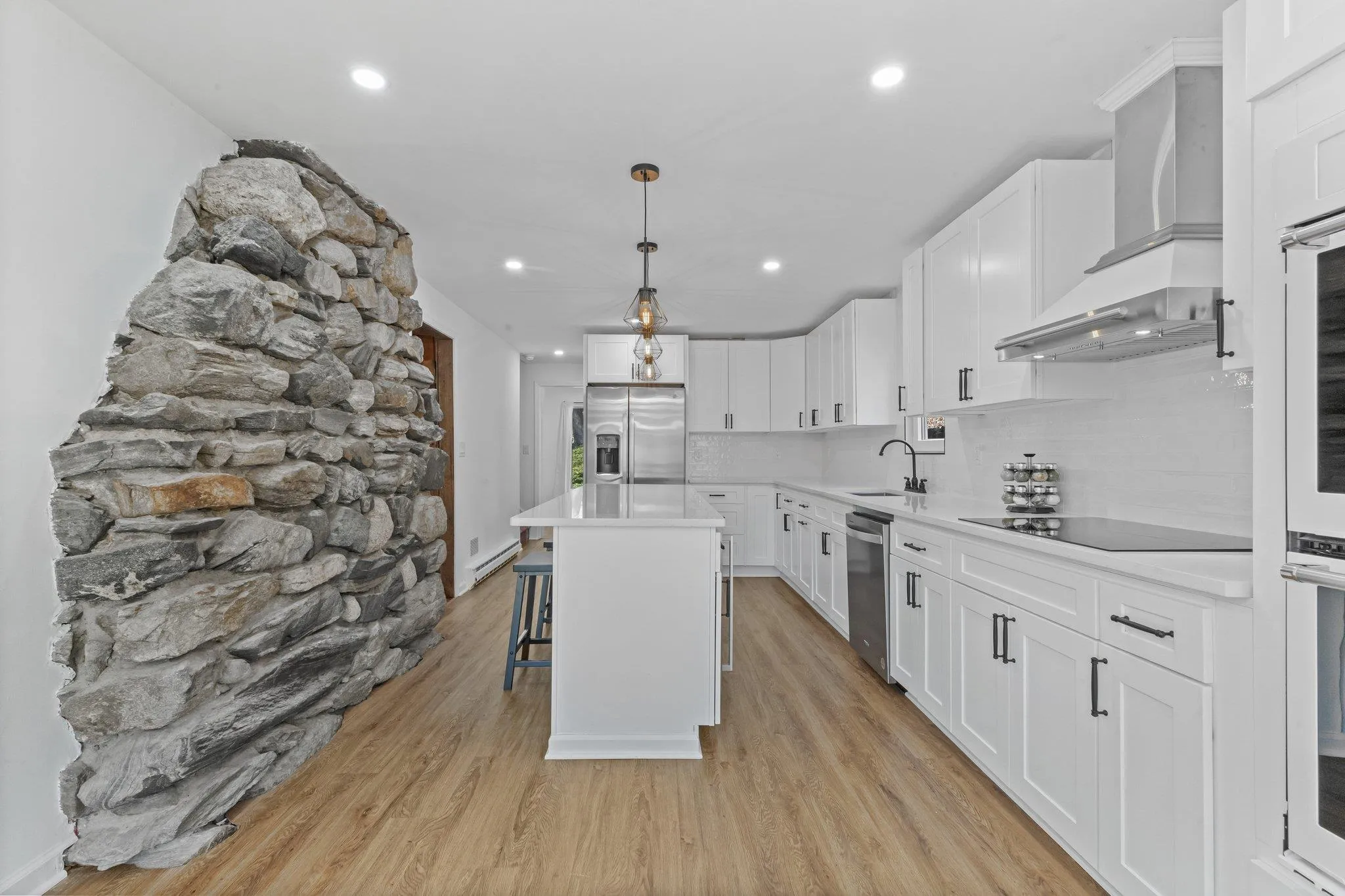 Kitchen with appliances with stainless steel finishes, wall chimney range hood, a breakfast bar area, white cabinets, and recessed lighting Kitchen with appliances with stainless steel finishes, wall chimney range hood, a breakfast bar area, white cabinets, and recessed lighting