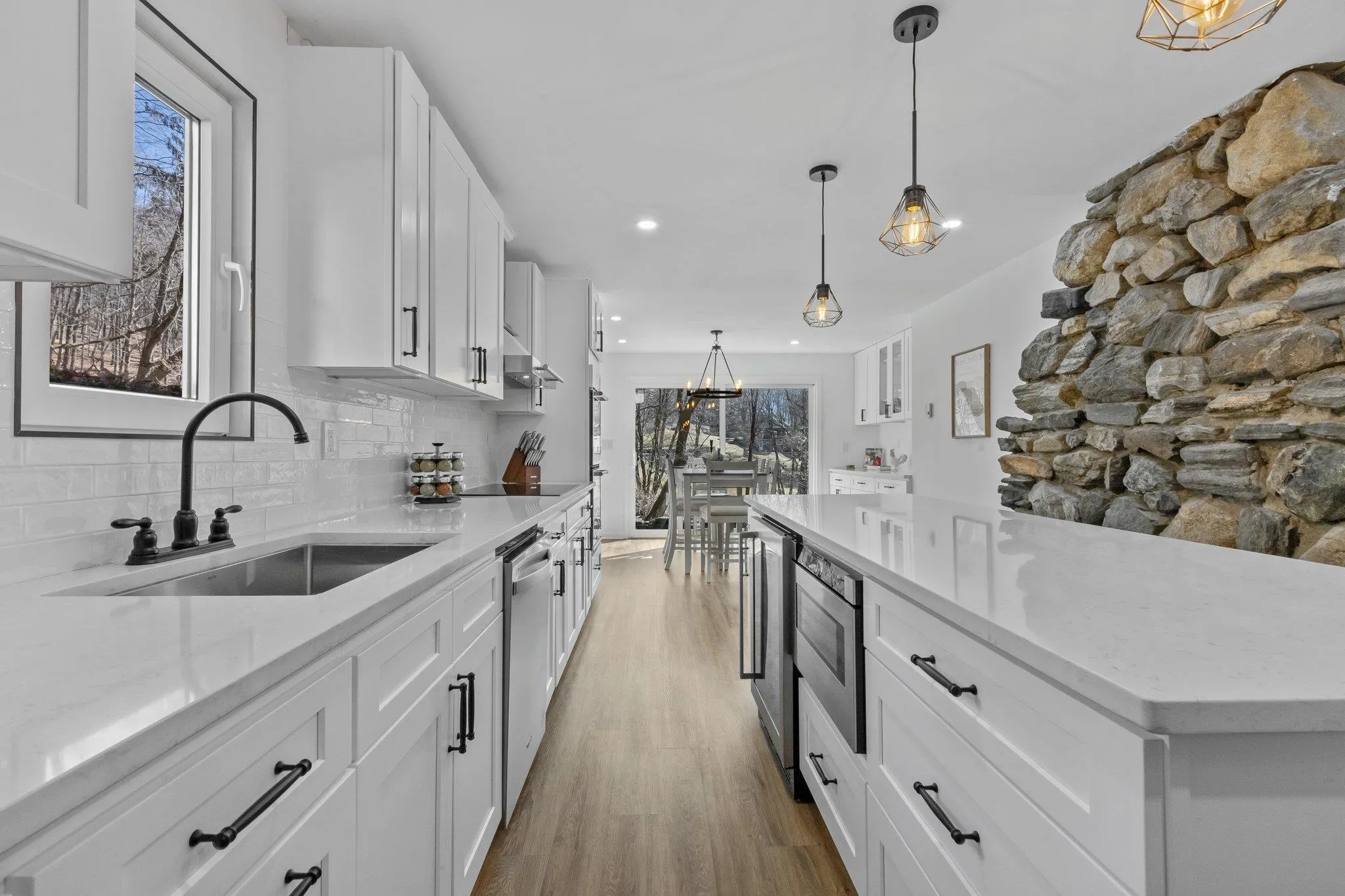 Kitchen featuring backsplash, stainless steel dishwasher, light wood finished floors, white cabinetry, and light stone countertops Kitchen featuring backsplash, stainless steel dishwasher, light wood finished floors, white cabinetry, and light stone countertops