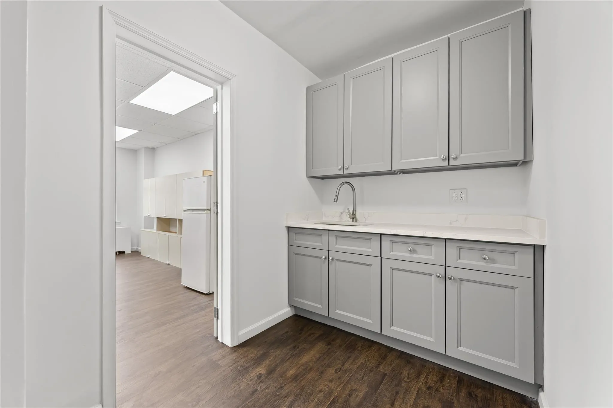 Kitchen featuring gray cabinets, freestanding refrigerator, dark wood-style flooring, and light countertops Kitchen featuring gray cabinets, freestanding refrigerator, dark wood-style flooring, and light countertops