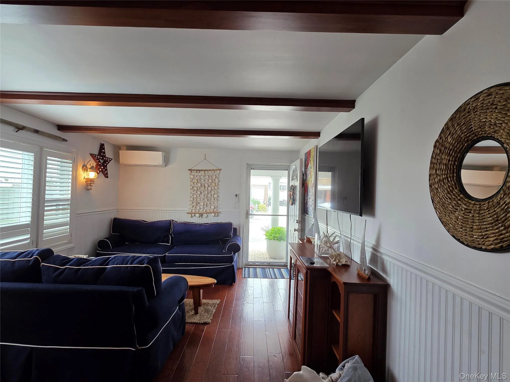 Living room featuring an AC wall unit, beamed ceiling, wainscoting, plenty of natural light, and dark wood-style flooring Living room featuring an AC wall unit, beamed ceiling, wainscoting, plenty of natural light, and dark wood-style flooring