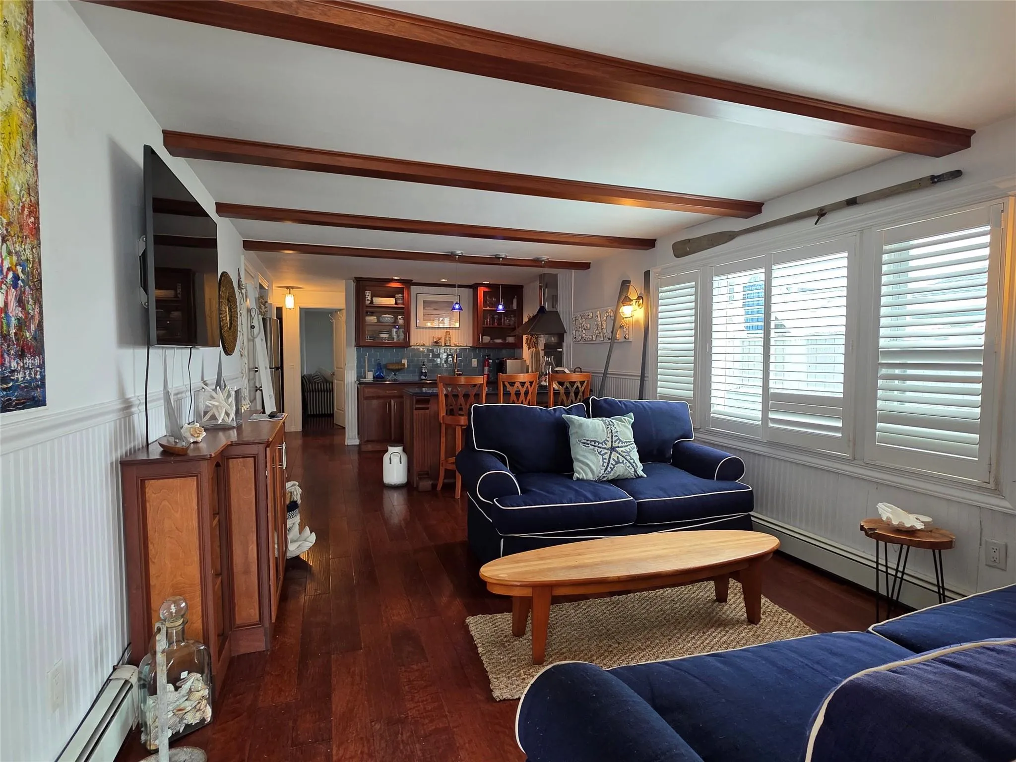 Living area with baseboard heating, beam ceiling, bar, dark wood finished floors, and a wainscoted wall Living area with baseboard heating, beam ceiling, bar, dark wood finished floors, and a wainscoted wall