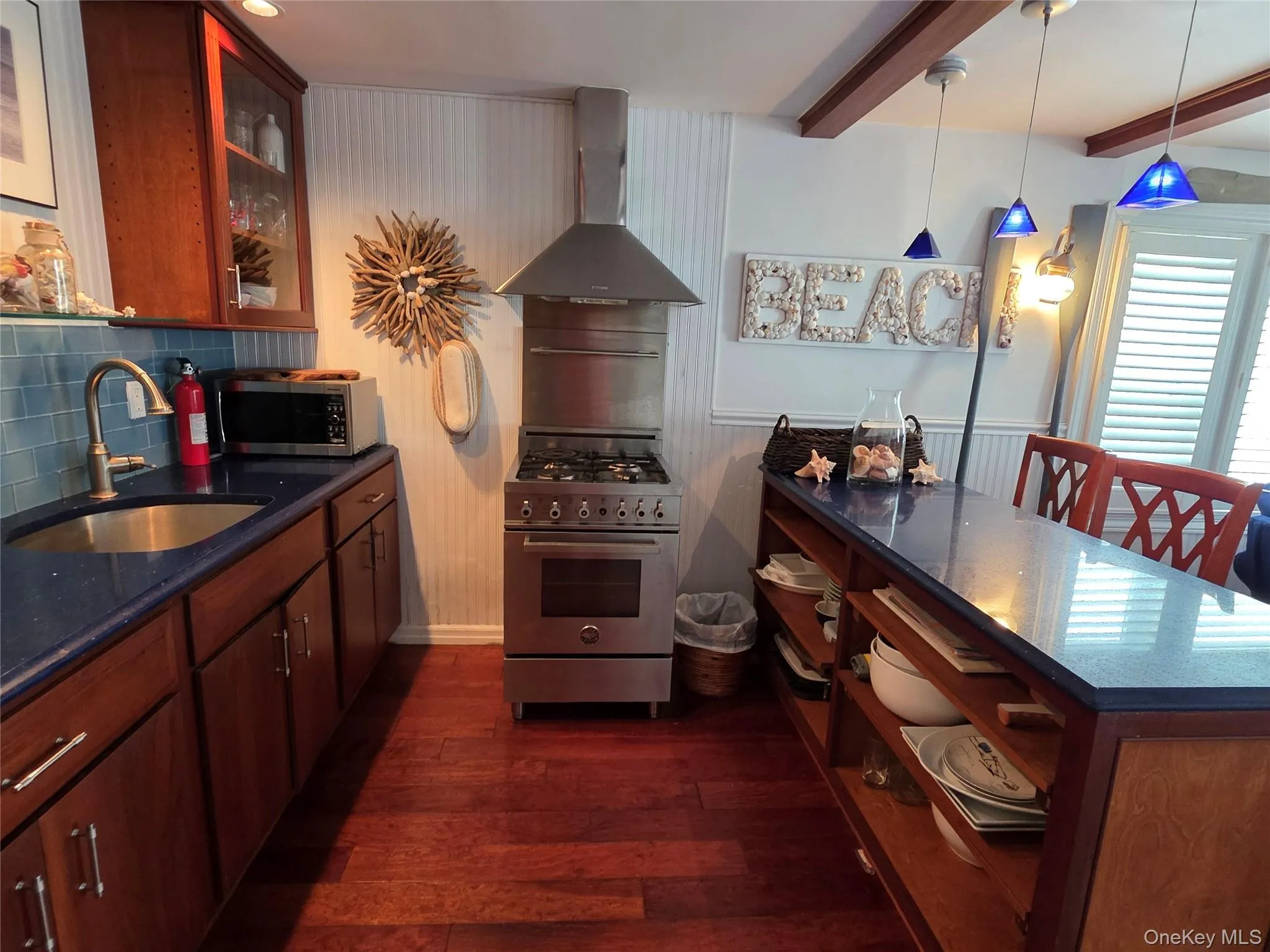 Kitchen with stainless steel appliances, wall chimney exhaust hood, dark wood-style floors, beam ceiling, and tasteful backsplash Kitchen with stainless steel appliances, wall chimney exhaust hood, dark wood-style floors, beam ceiling, and tasteful backsplash