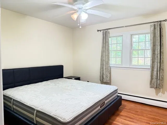 Bedroom with wood finished floors, a baseboard radiator, and a ceiling fan Bedroom with wood finished floors, a baseboard radiator, and a ceiling fan
